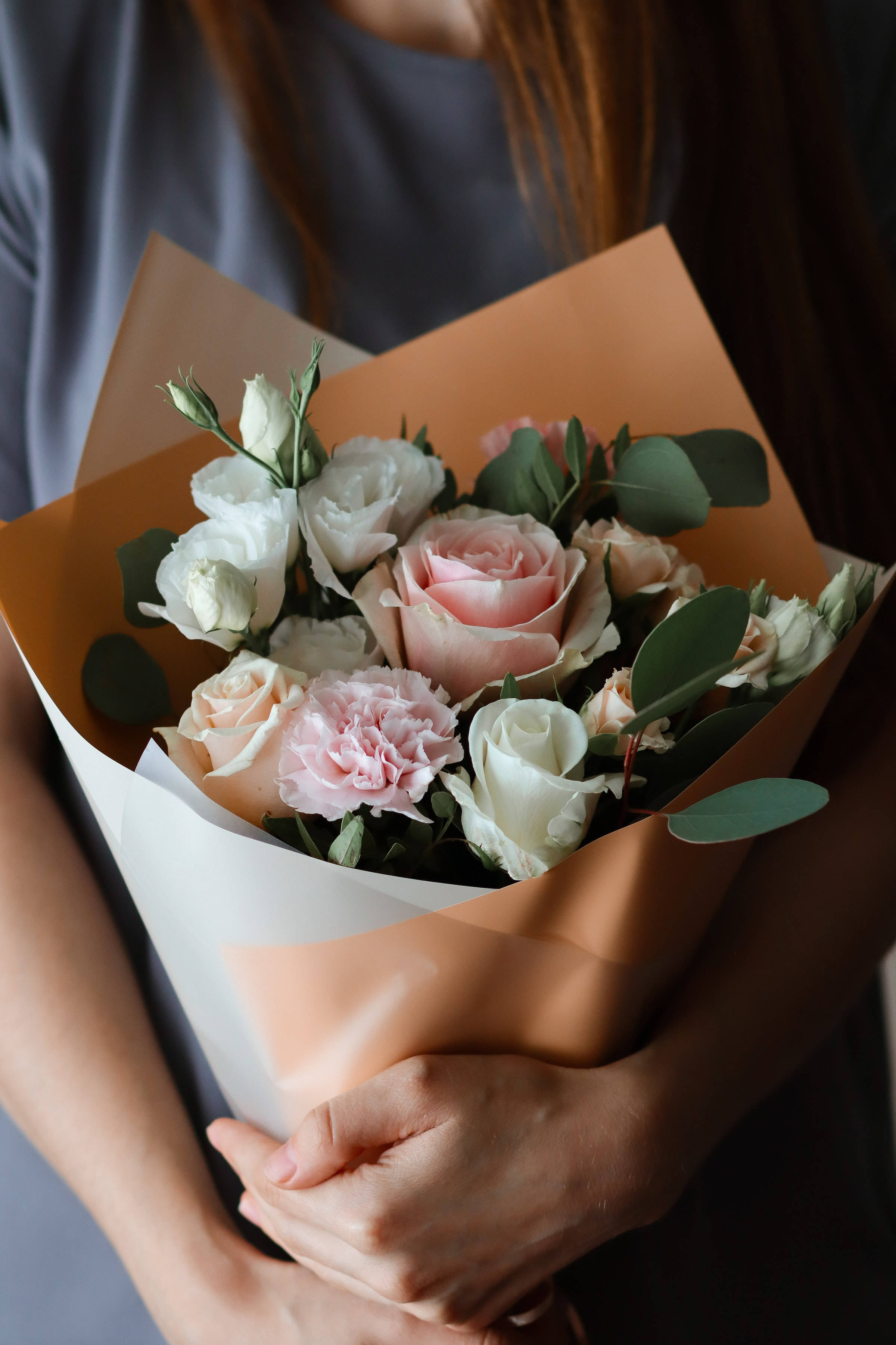 Bouquet 桌布 壁紙 — 一個人懷抱著一束柔和的粉彩色玫瑰和康乃馨花束，包裹在蜜桃色和白色的紙張中。