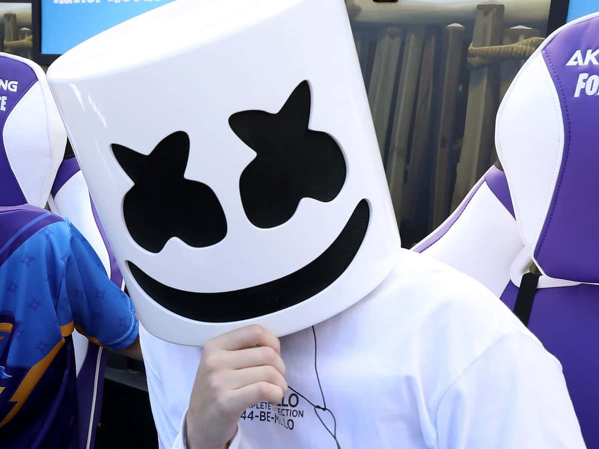 Marshmello 動態圖 桌布 壁紙 — 一個人戴著一個帶有黑色笑臉圖案的大型白色棉花糖頭盔，坐在一張紫色電競椅上。