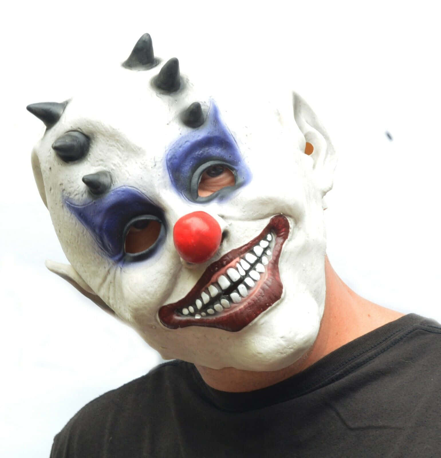 Creepy Halloween 桌布 壁紙 — 一個人戴著一個怪誕的小丑面具，帶有黑色尖刺、藍色眼妝、紅色鼻子和露齒大笑，背景是純白色。