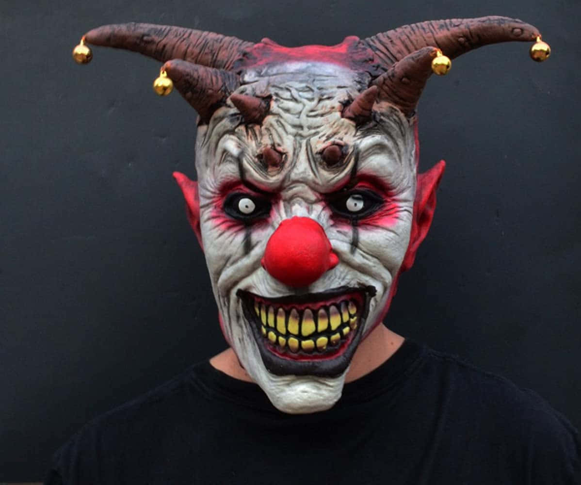 Creepy Halloween 桌布 壁紙 — 一個人戴著一個怪誕的小丑面具，有角、金色鈴鐺、紅鼻子和尖牙，背景是深色的。