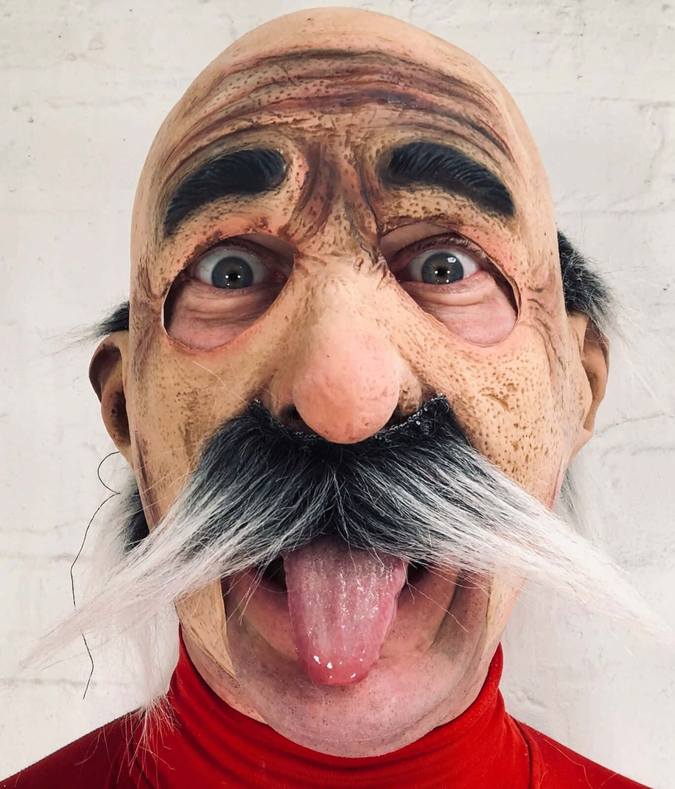 Mask 桌布 壁紙 — 一個人戴著一個怪誕的橡膠面具，面具是一個長著白色長鬍鬚、伸出舌頭的老人，背景是白色磚牆。