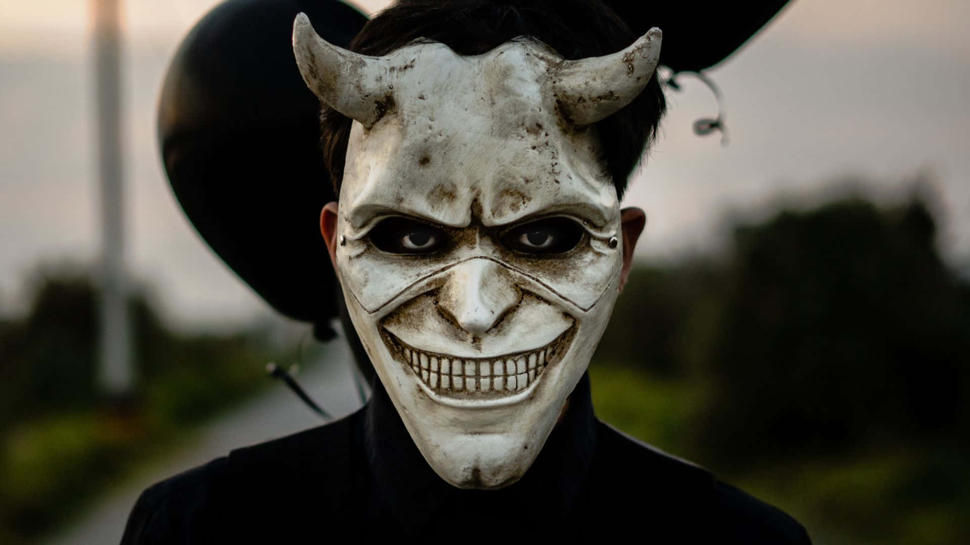 Horror Masks 桌布 壁紙 — 一個人戴著一個破舊的白色魔鬼面具，有角和咧嘴笑，背景是模糊的戶外環境。