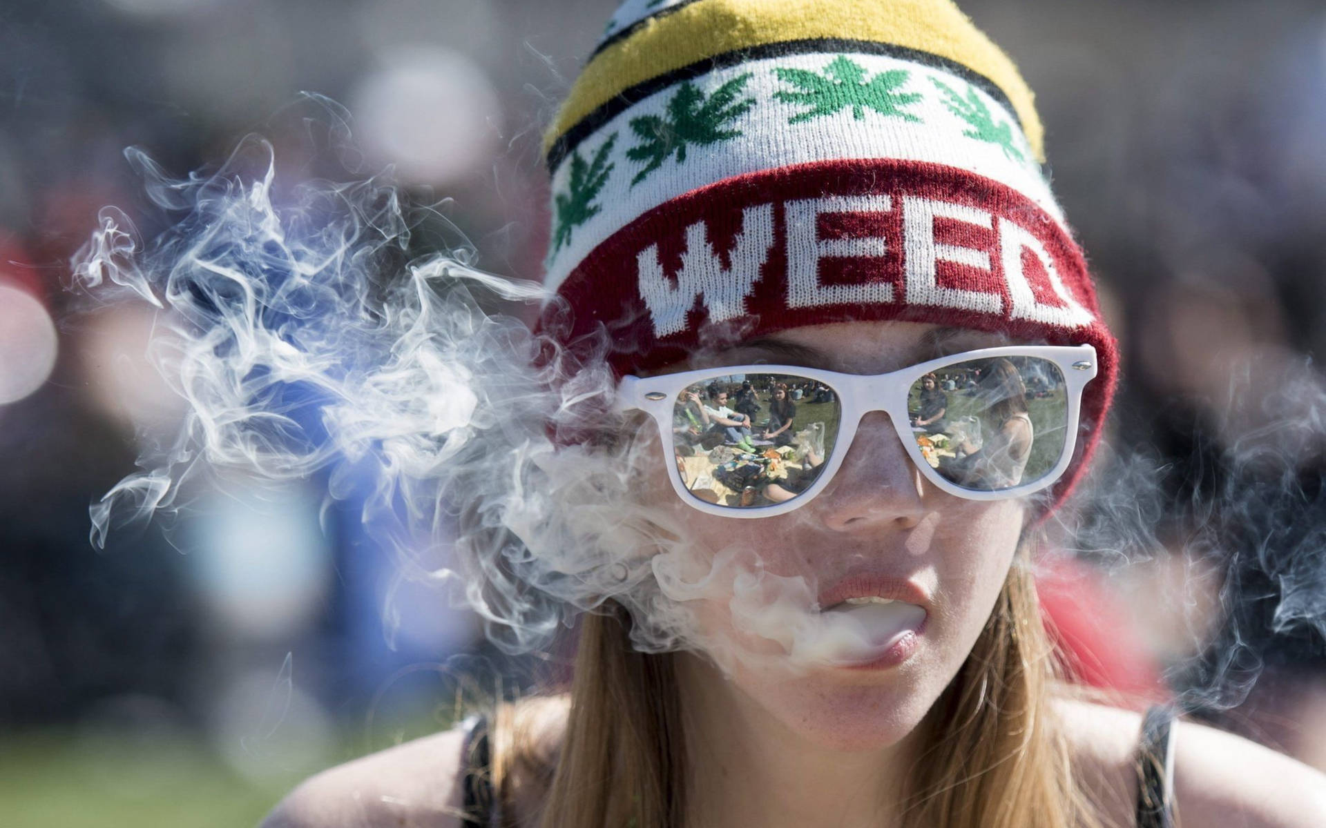 戴著weed毛帽和太陽眼鏡的人在戶外活動中呼出煙霧。