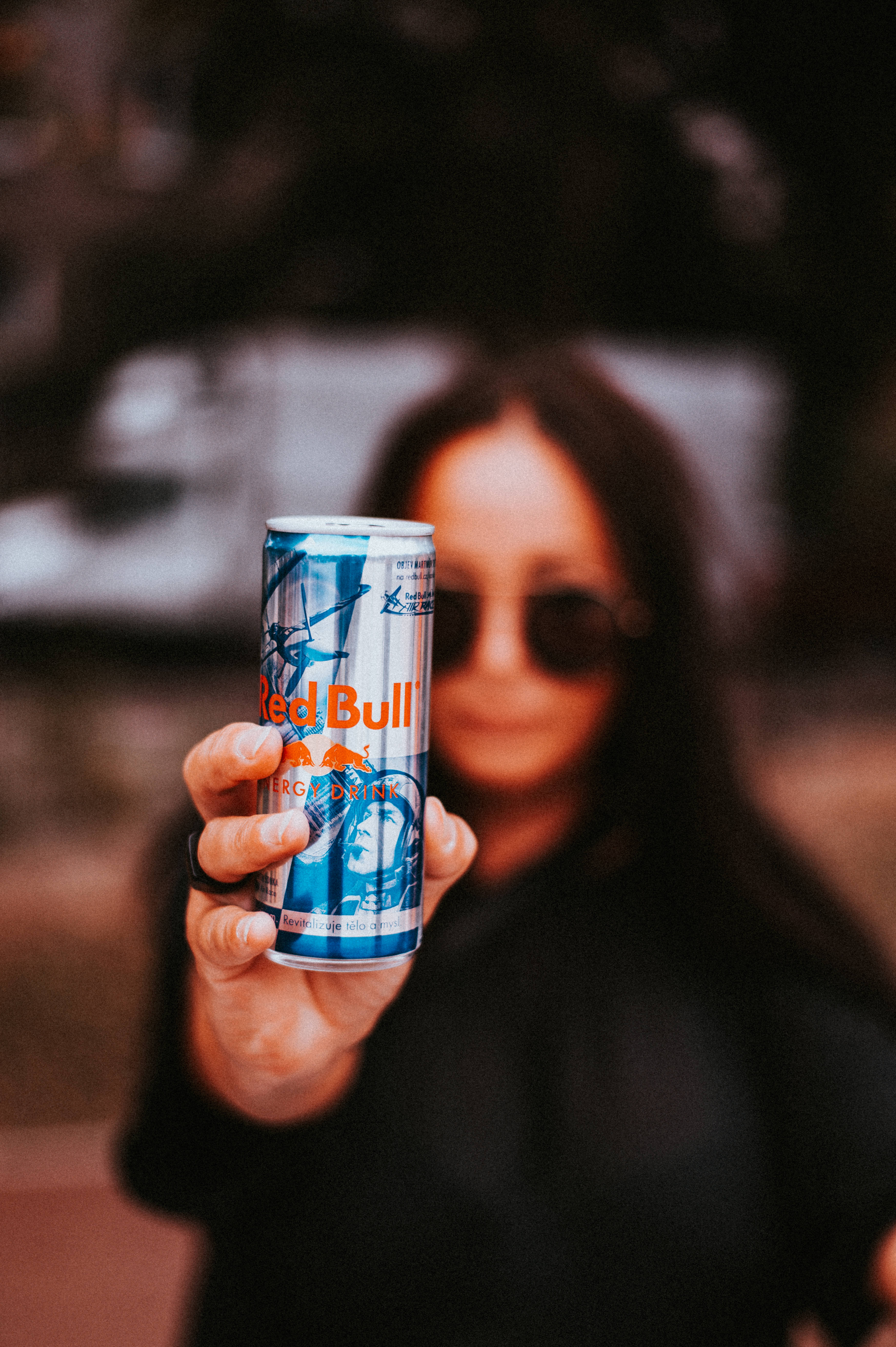 bull 桌布 壁紙 — 一個人戴著太陽眼鏡，在淺景深鏡頭中將紅牛罐向前遞。