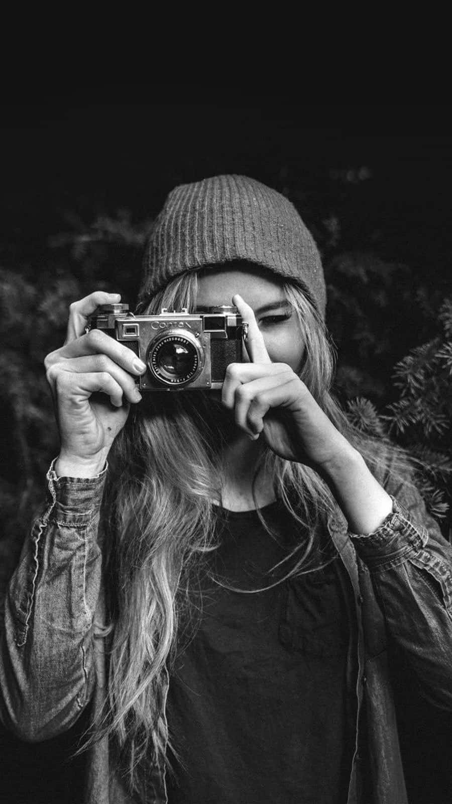 Woman 桌布 壁紙 — 一個人戴著毛帽，在黑暗模糊的背景前將一部復古相機舉到臉前。