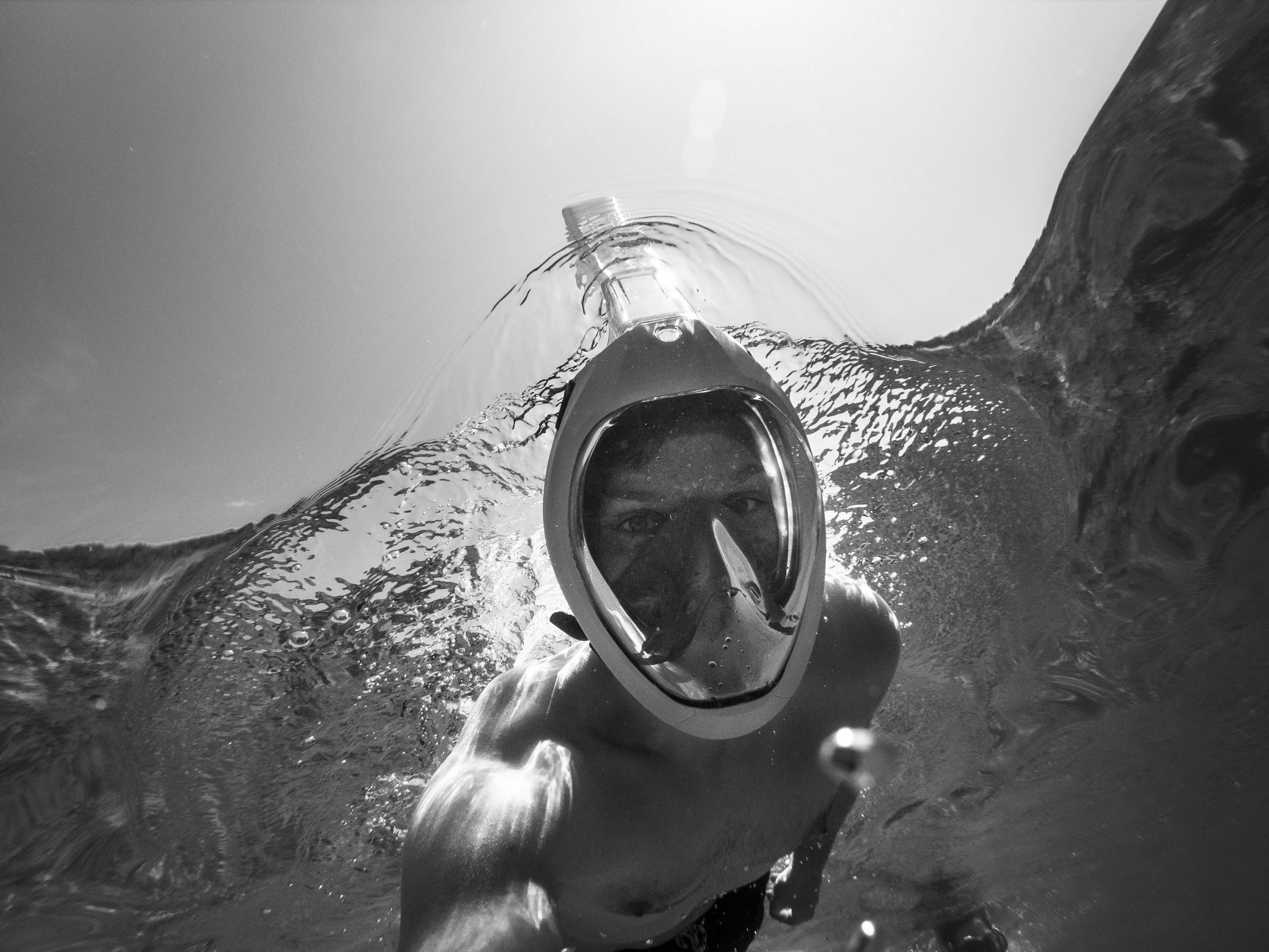Snorkeling 桌布 壁紙 — 一個人戴著潛水面罩從洶湧的水中浮出，陽光穿透水面。