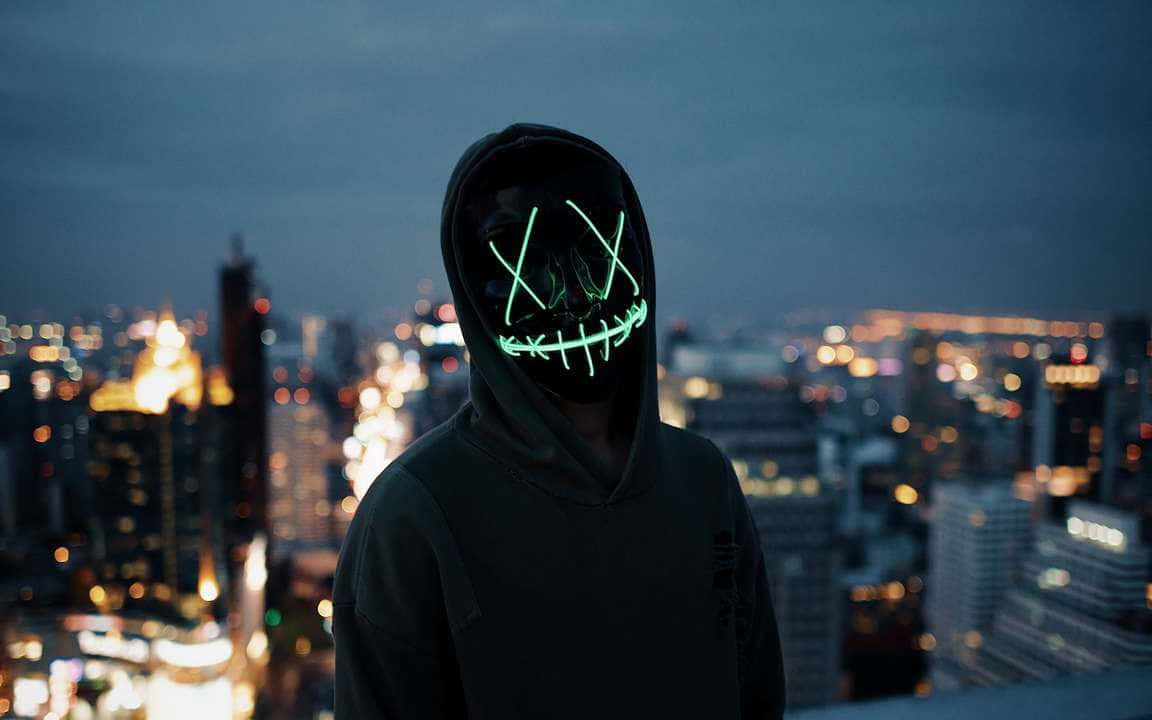 Mask 桌布 壁紙 — 一個人戴著發光的綠色骷髏面具，站在城市頂端，夜晚下方有模糊的燈光。