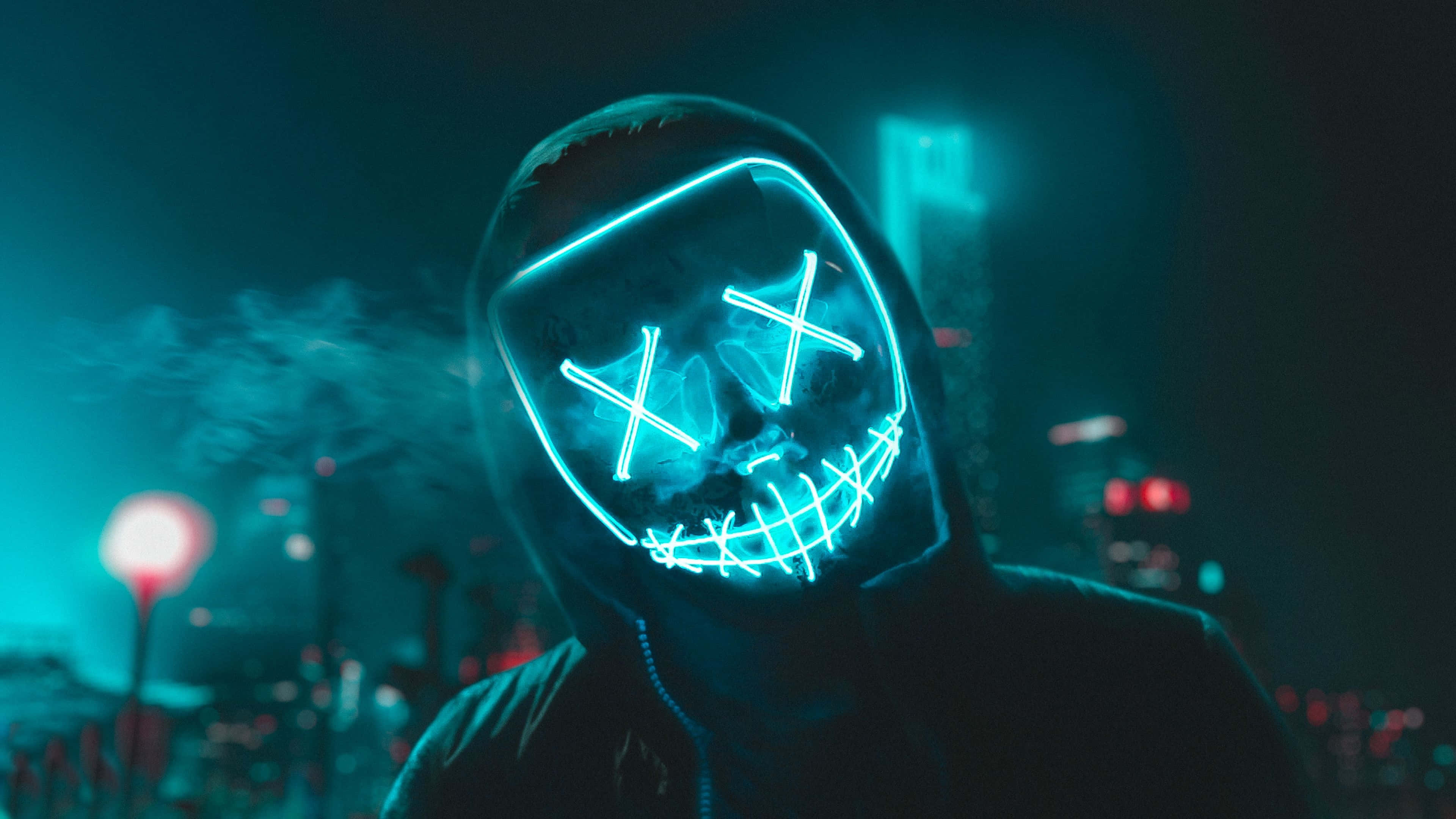 Mask 桌布 壁紙 — 一個人戴著發光的藍色LED骷髏面具，在夜晚霓虹燈閃爍的城市景觀中呼出煙霧。
