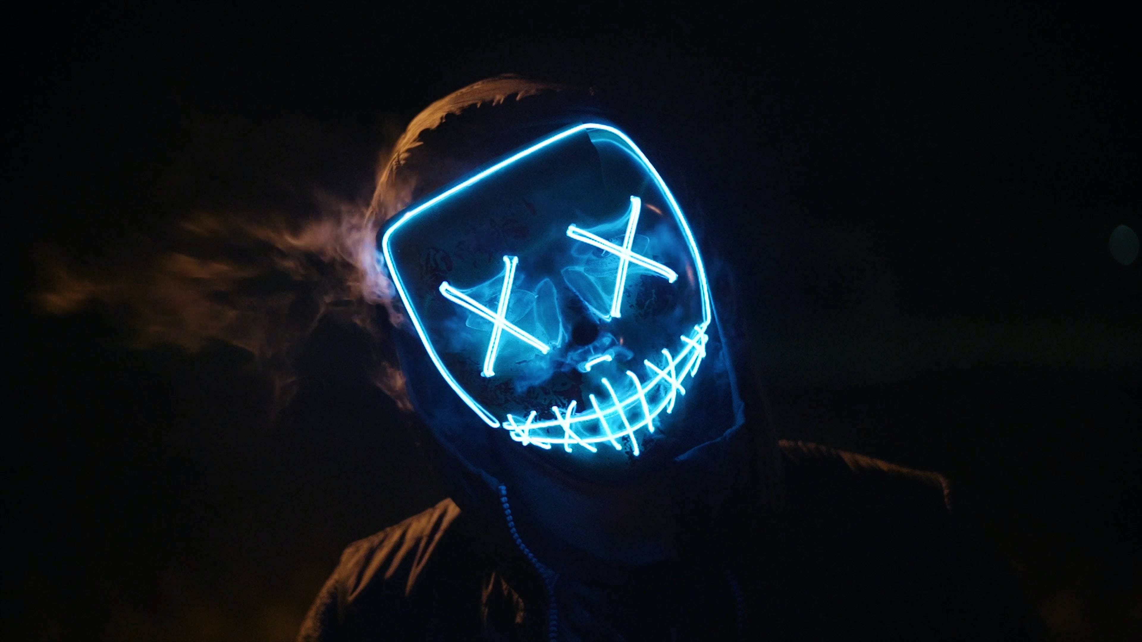 evil smile 桌布 壁紙 — 一個人戴著發光藍色LED面具，眼睛呈X形，嘴巴縫合，在黑暗背景下呼出煙霧。