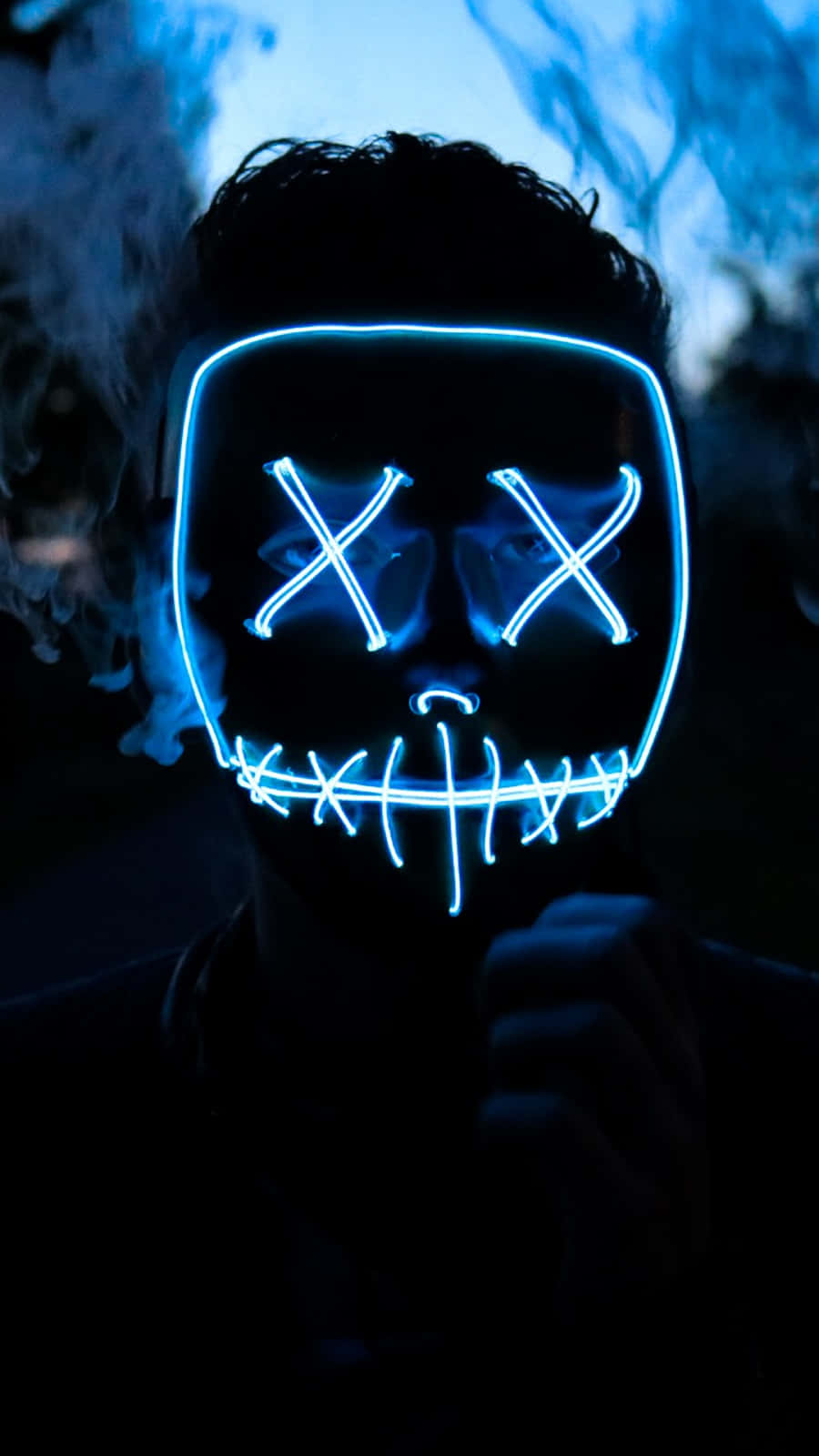 Cool Art Phone 桌布 壁紙 — 一個人戴著發光藍色LED面具，面具上有X形眼睛和縫合的嘴巴，背景是煙霧瀰漫的黑暗環境。