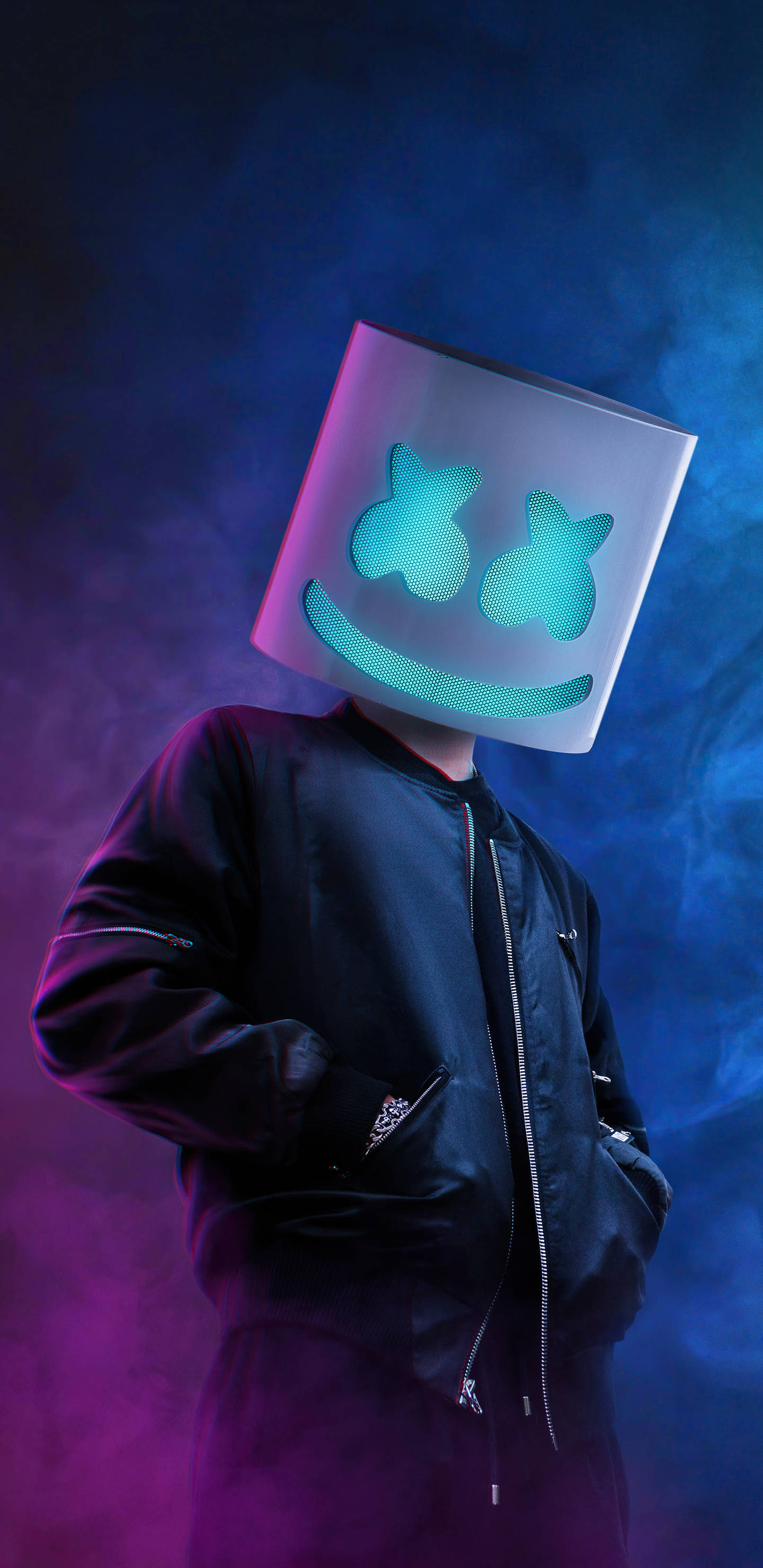 marshmello iPhone 桌布 壁紙 — 一個人戴著發光藍色笑臉面具，站在煙霧彌漫的紫色和藍色燈光中，身穿黑色轟炸機夾克。