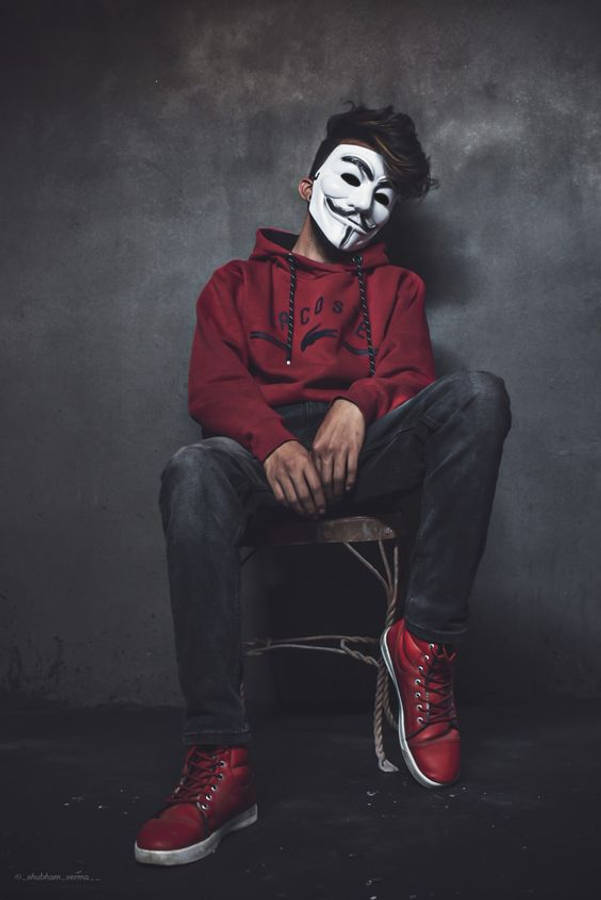 bad 桌布 壁紙 — 一個人戴著白色 Guy Fawkes 面具，坐在木凳上，背景是深灰色牆壁，身穿紅色連帽衫和相配的紅色運動鞋。
