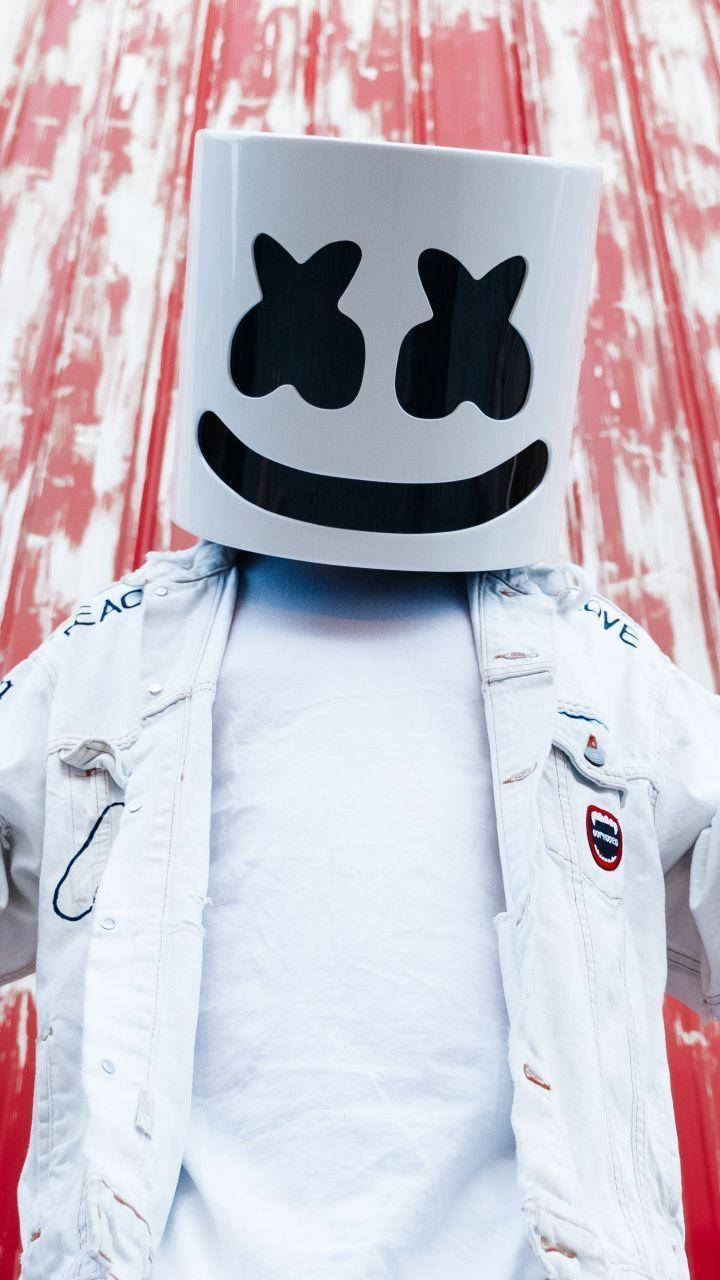 marshmello iPhone 桌布 壁紙 — 一個人戴著白色Marshmello頭盔，站在風化的紅白木牆前。