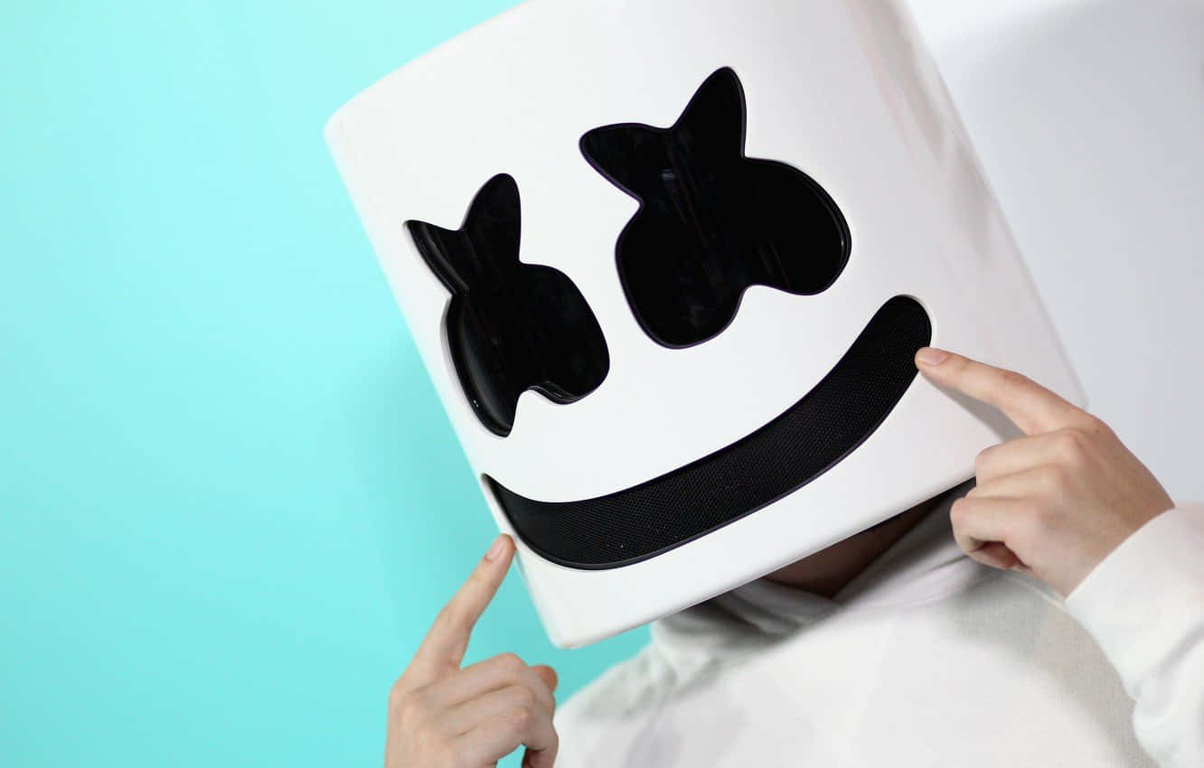 Marshmello 動態圖 桌布 壁紙 — 一個人戴著白色Marshmello頭盔，上面有黑色笑臉，在藍綠色背景上指向它。