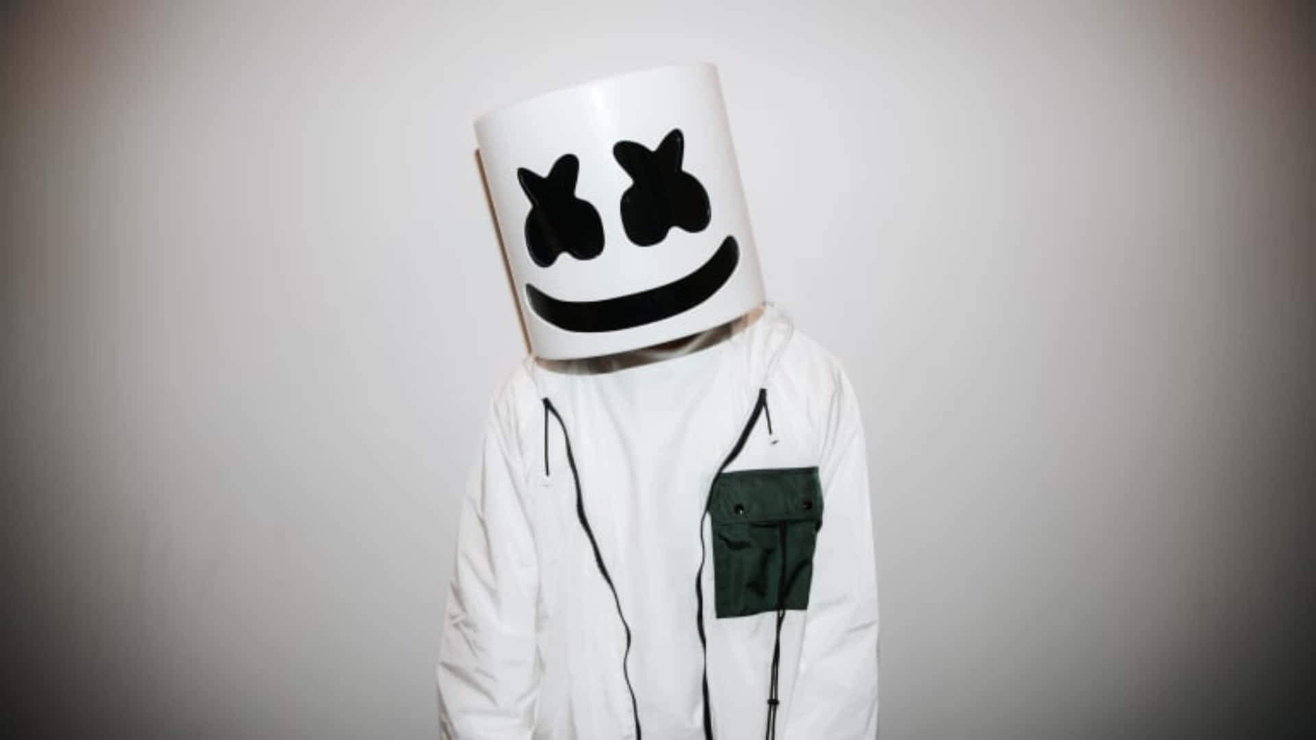 Marshmello 動態圖 桌布 壁紙 — 一個人戴著白色棉花糖頭盔，上面有黑色笑臉，站在純灰色背景前，穿著帶有綠色口袋的白色外套。