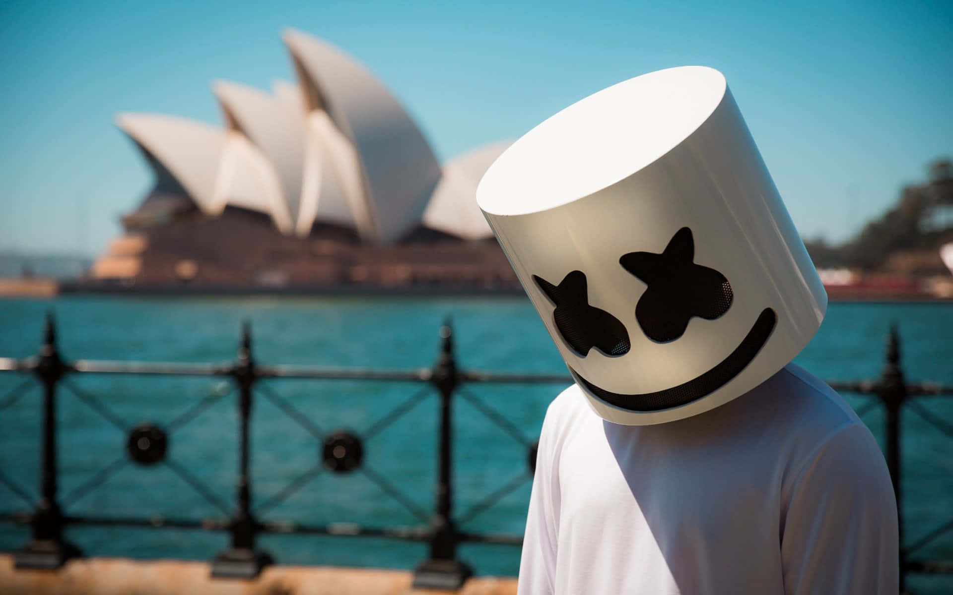 Marshmello 動態圖 桌布 壁紙 — 一個人戴著白色棉花糖頭盔，站在晴朗藍天下標誌性的雪梨歌劇院前。