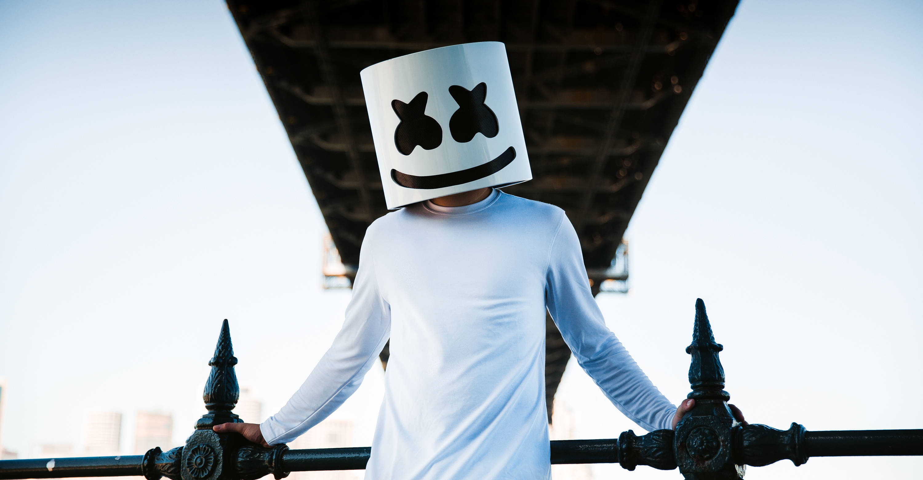 Marshmello 動態圖 桌布 壁紙 — 一個人戴著白色棉花糖頭盔，站在橋樑欄杆上，背景是明亮的天空。
