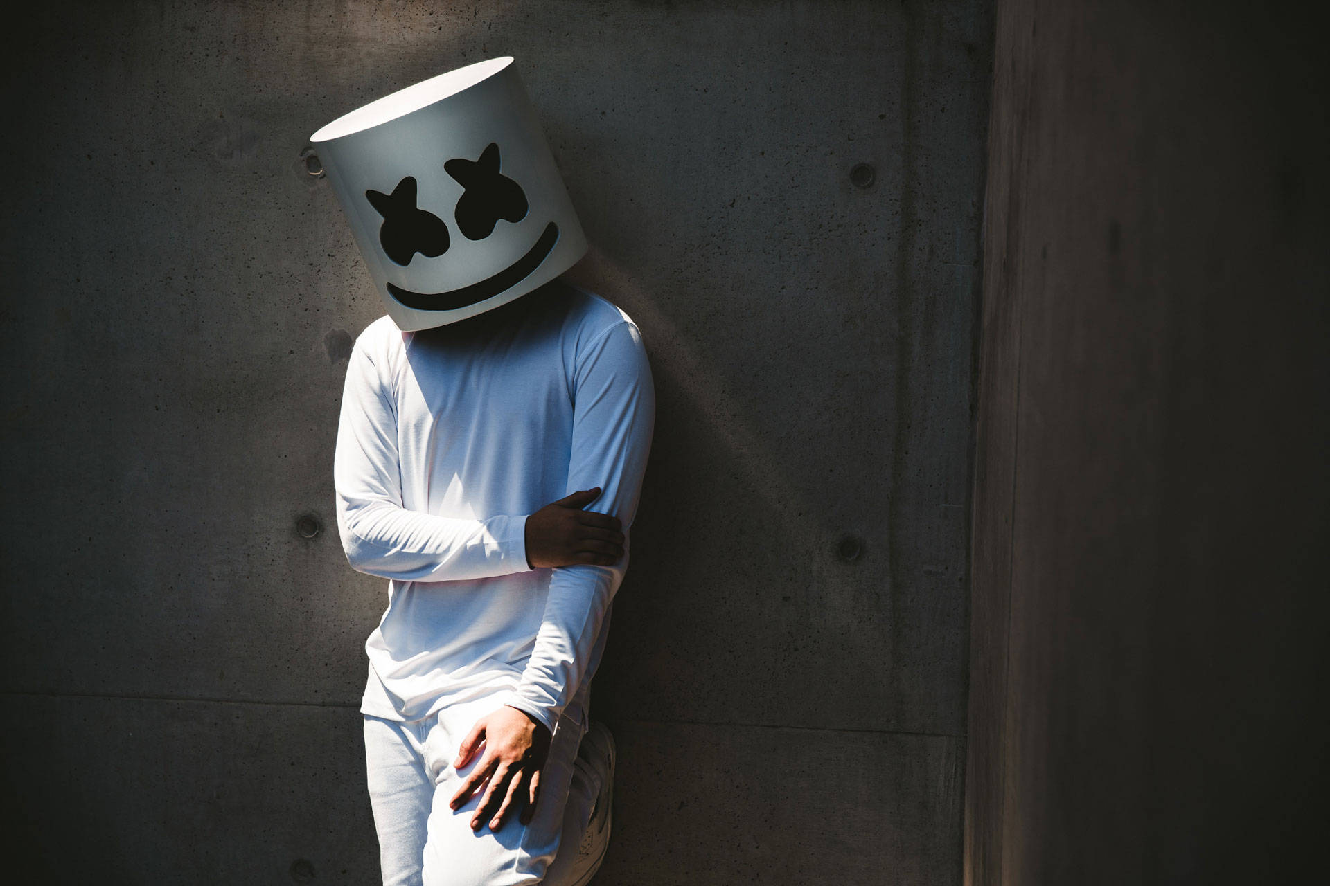Marshmello 動態圖 桌布 壁紙 — 一個人戴著白色棉花糖頭盔，靠在沐浴在明亮陽光下的混凝土牆上。