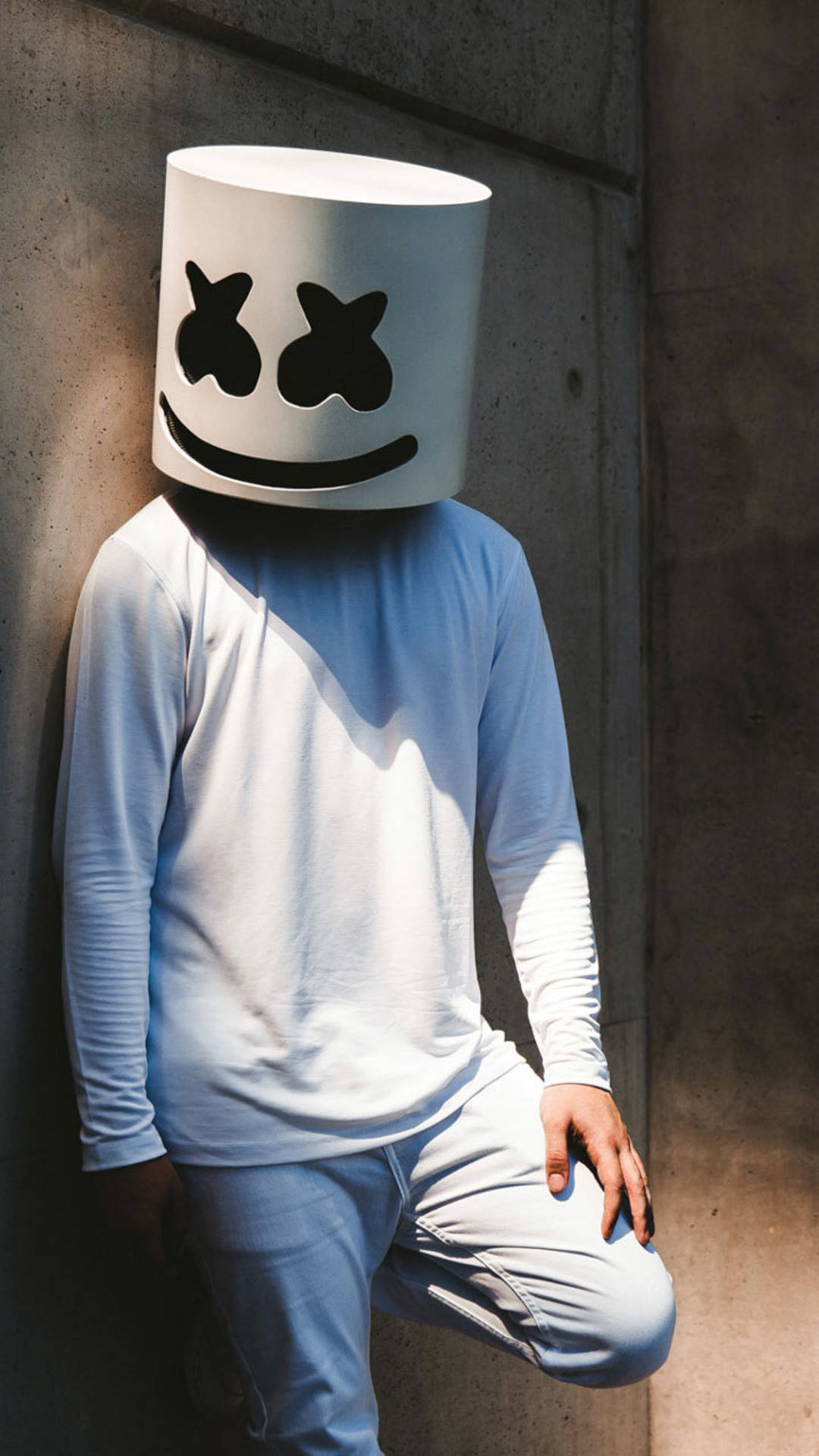 Marshmello 動態圖 桌布 壁紙 — 一個人戴著白色棉花糖頭盔，靠著沐浴在明亮陽光下的混凝土牆。