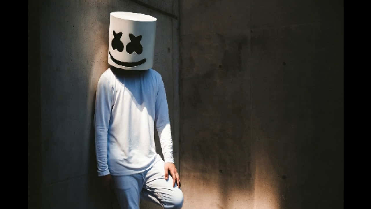 Marshmello 動態圖 桌布 壁紙 — 一個人戴著白色棉花糖頭盔，面帶微笑，靠著混凝土牆，沐浴在斑駁的陽光下。