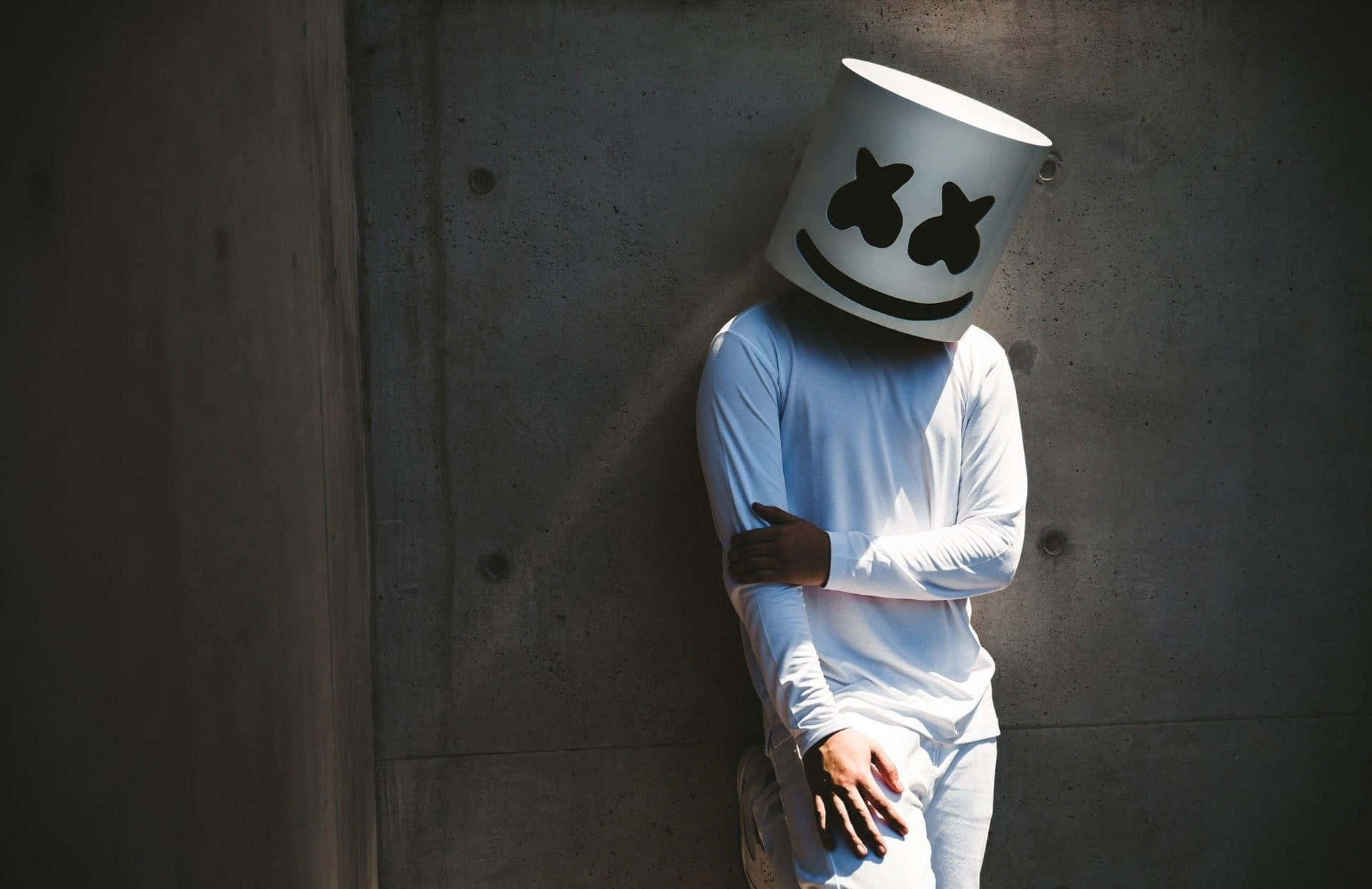 Marshmello 動態圖 桌布 壁紙 — 一個人戴著白色笑臉漁夫帽，在柔和日光下靠著混凝土牆。