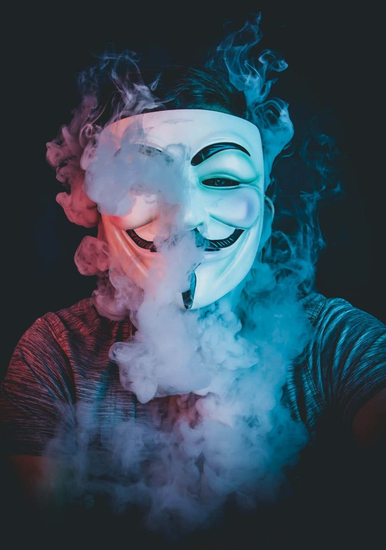 Cool Profile 桌布 壁紙 — 一個人戴著白色蓋伊·福克斯面具，在霓虹藍和粉紅色調照亮的黑暗背景下呼出旋轉的煙霧。