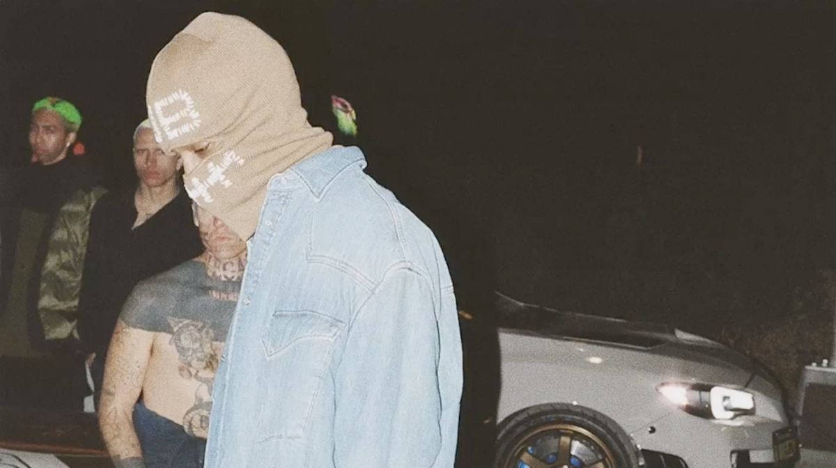  壁紙 — 一個人戴著米色毛帽和牛仔外套，夜晚站在一輛銀色車前面，附近有另外兩個人。