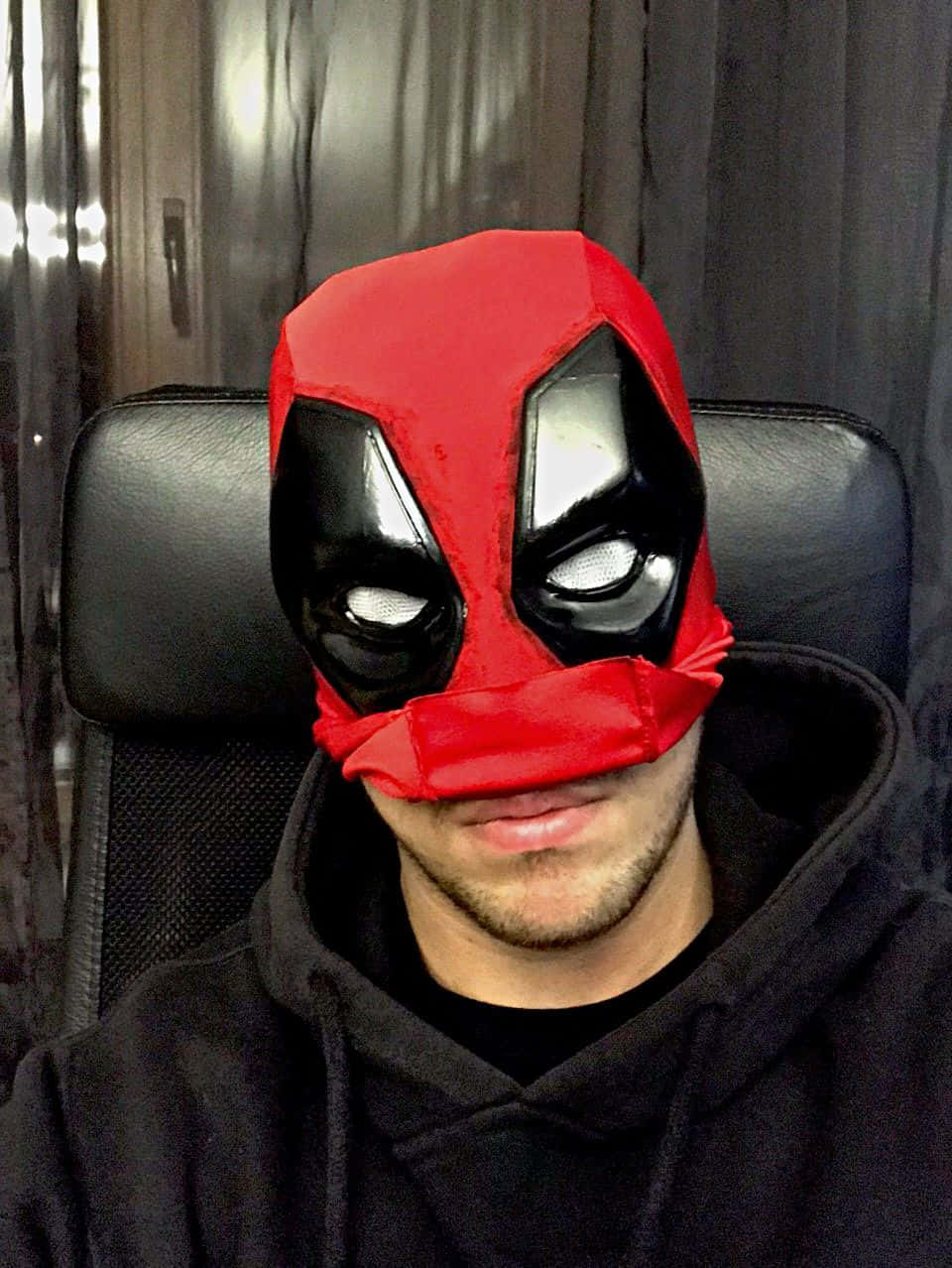 Deadpool Mask 桌布 壁紙 — 一個人戴著紅黑色死侍面具，坐在黑色辦公椅上，背景是深色窗簾。
