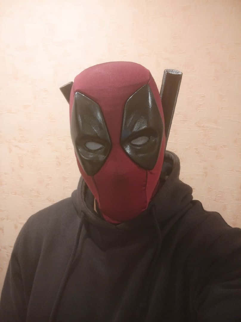 Deadpool Mask 桌布 壁紙 — 一個人戴著紅黑色死侍面具，背上綁著兩把武士刀，站在米白色牆前。