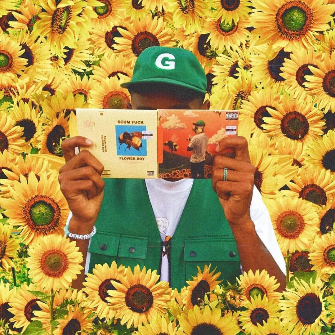 Sunflower Aesthetic 桌布 壁紙 — 一個人戴著綠色帽子和背心，站在充滿活力的向日葵田中，手持兩張專輯封面。