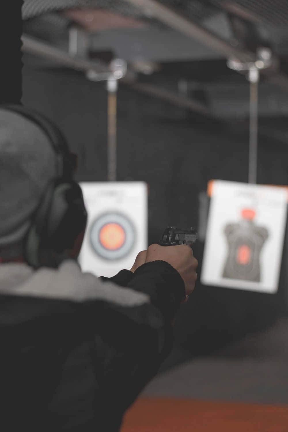 Shooting 桌布 壁紙 — 一個人戴著耳罩在光線昏暗的室內射擊場用手槍瞄準目標。