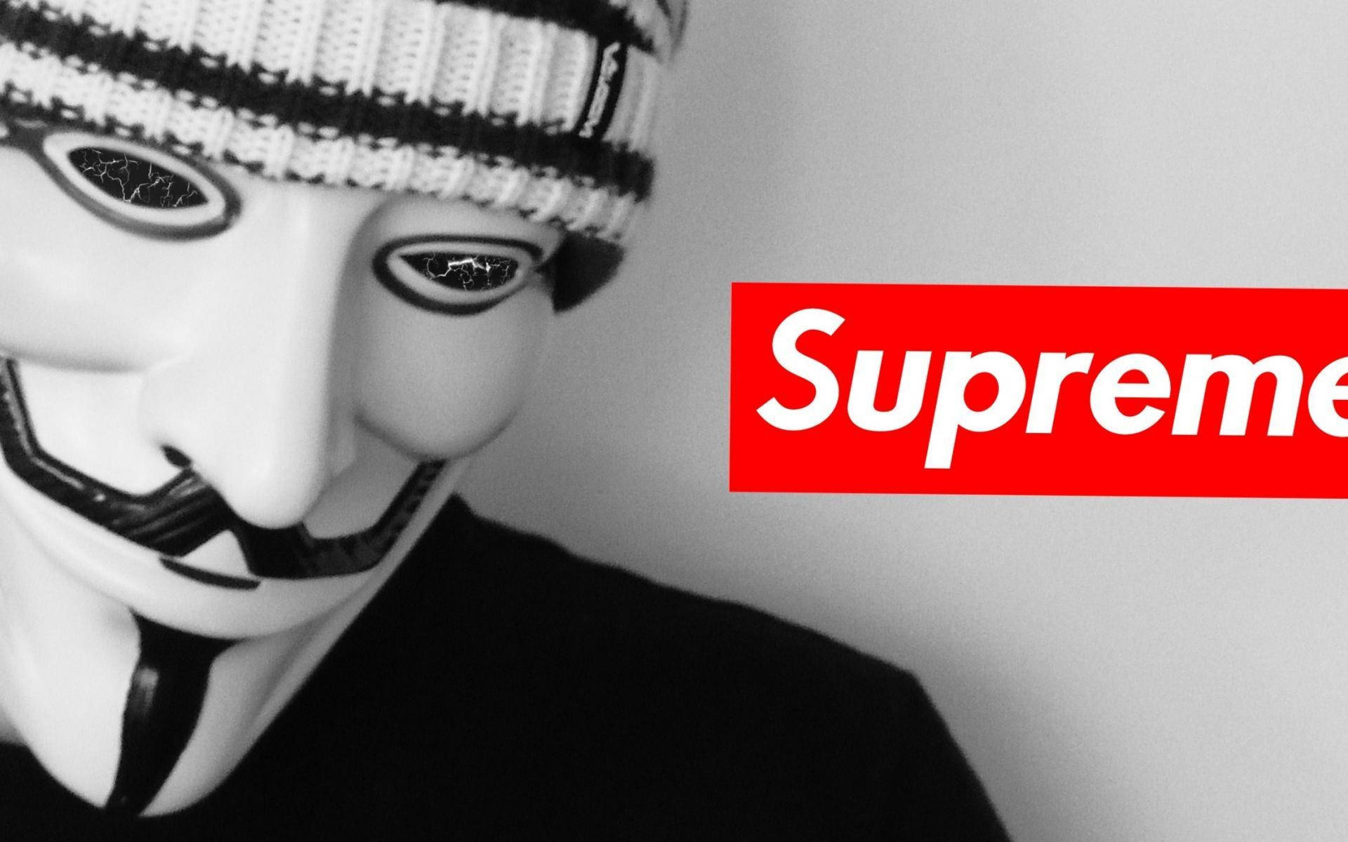 戴著蓋伊·福克斯面具和毛帽的人站在 Supreme 標誌旁邊。