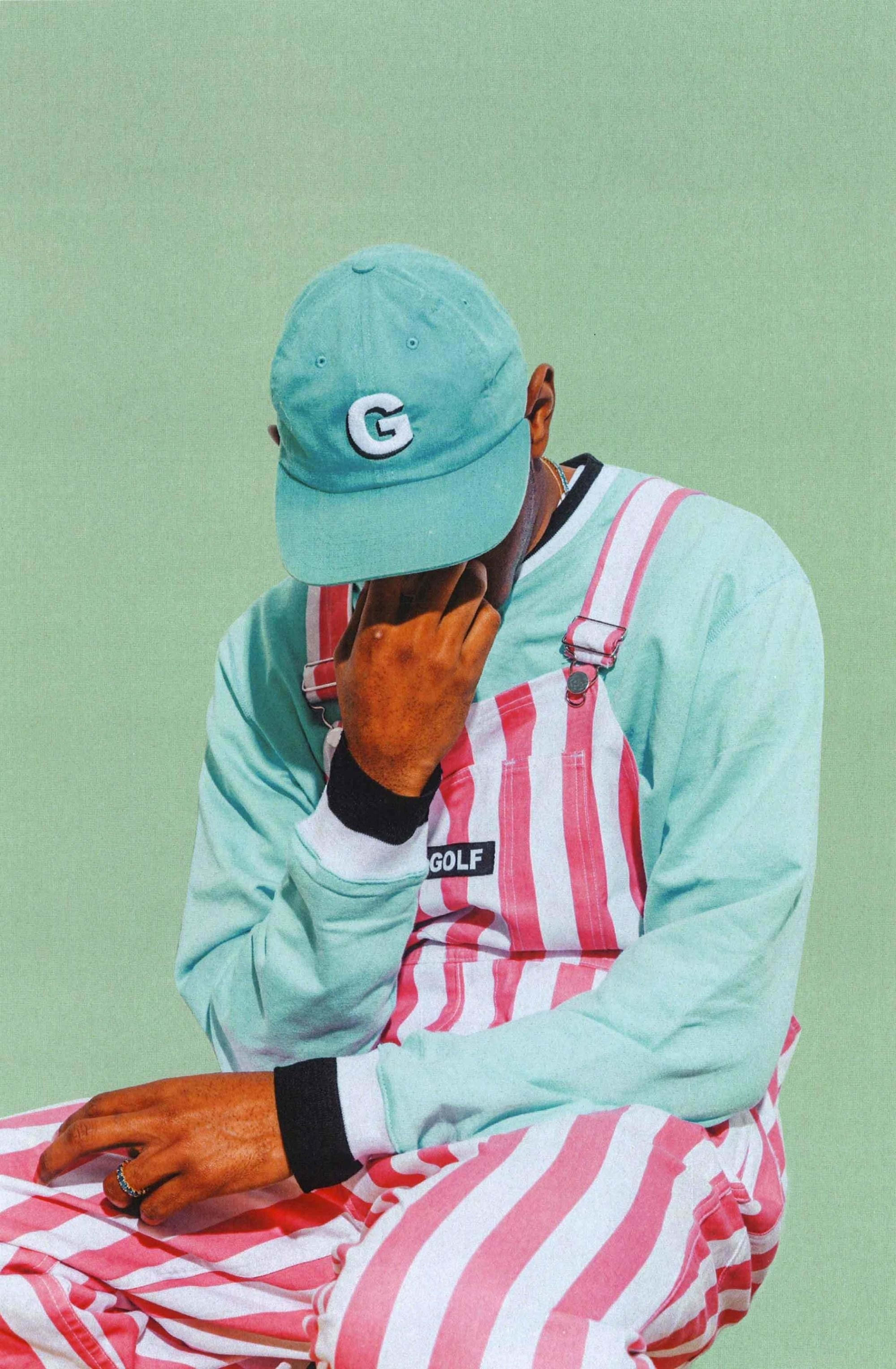 Tyler The Creator 4K 桌布 壁紙 — 一個人戴著薄荷綠色帽子和粉紅色條紋連身褲，坐在純薄荷綠色背景前，用手遮住臉。