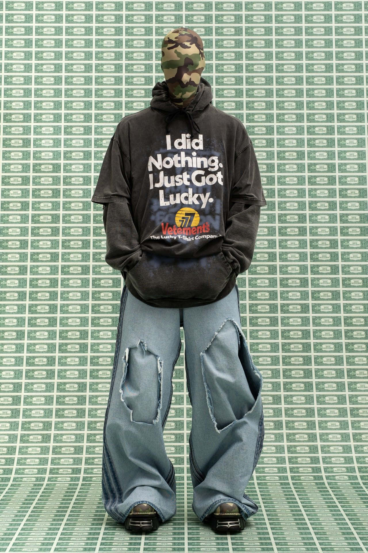 vetements 桌布 壁紙 — 一個人戴著迷彩頭套和超大連帽衫，站在綠色美元鈔票圖案背景前。