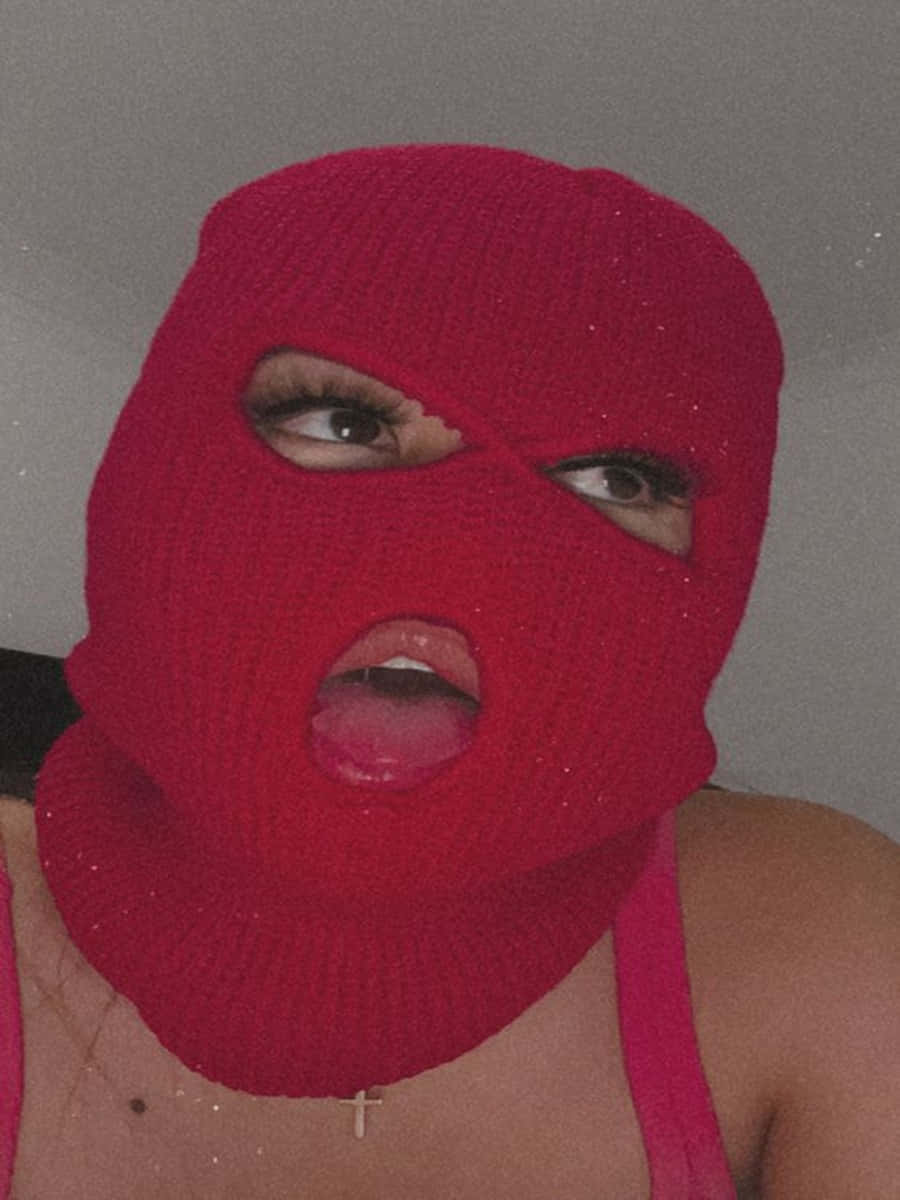 Ski Mask Girl 桌布 壁紙 — 一個人戴著閃亮紅色針織巴拉克拉法帽，有眼睛和嘴巴的開口，背景是純灰色牆壁。