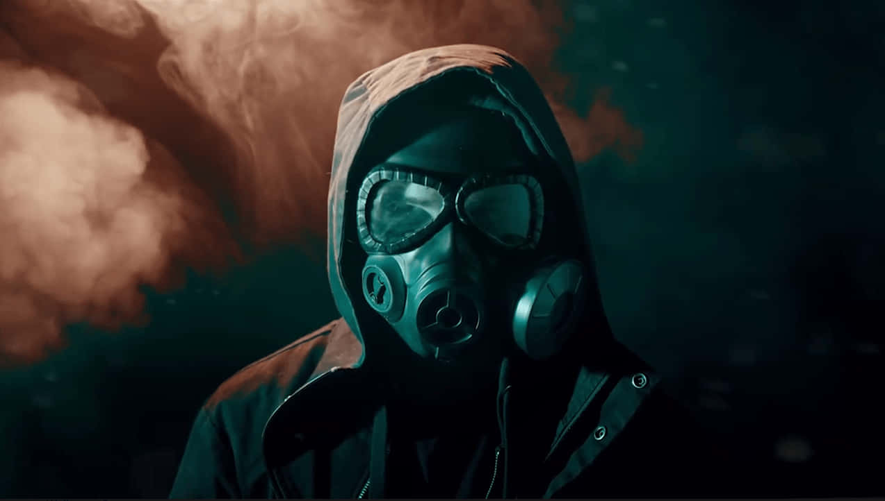 Mask Boy 桌布 壁紙 — 一個人戴著防毒面具和兜帽，站在黑暗、不祥的環境中，周圍是旋轉的橙色和藍綠色煙霧。