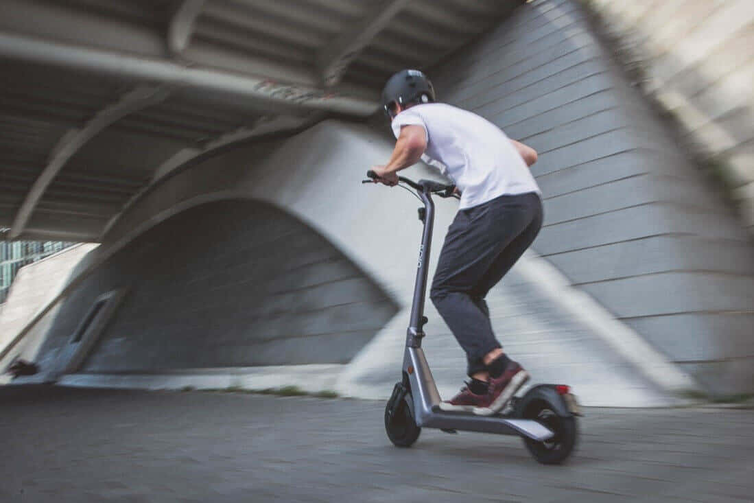 scooter 桌布 壁紙 — 一個人戴著頭盔在混凝土天橋下騎電動滑板車，動態模糊傳達速度感。