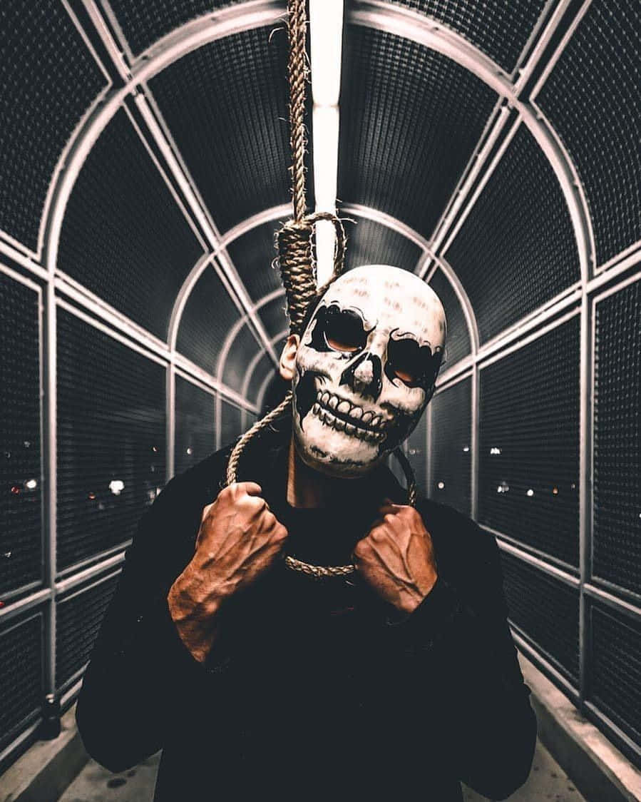 Mask 桌布 壁紙 — 一個人戴著骷髏面具，抓住一條從金屬拱形天花板垂下的繩索，在燈光昏暗的隧道中。