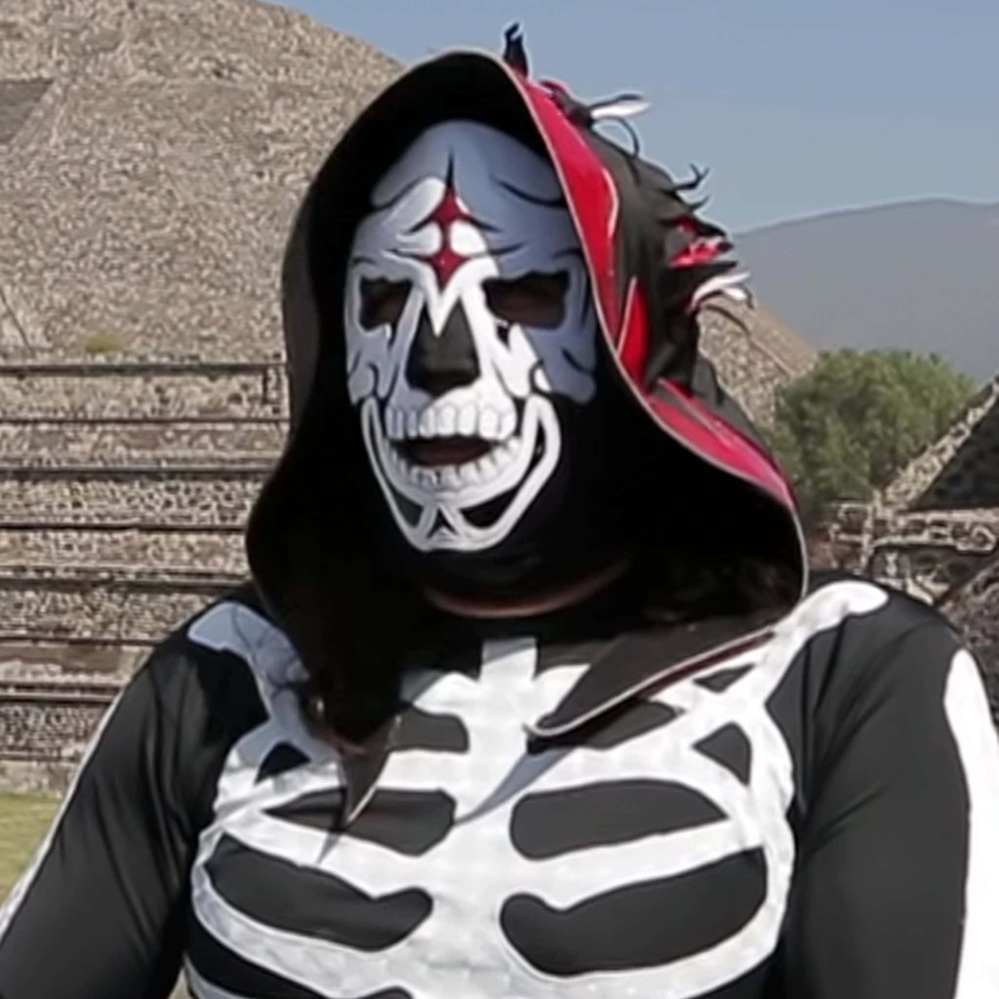 La Parka 桌布 壁紙 — 一個人戴著骷髏面具、穿著骷髏服裝，站在晴朗天空下的古老石頭廢墟前。