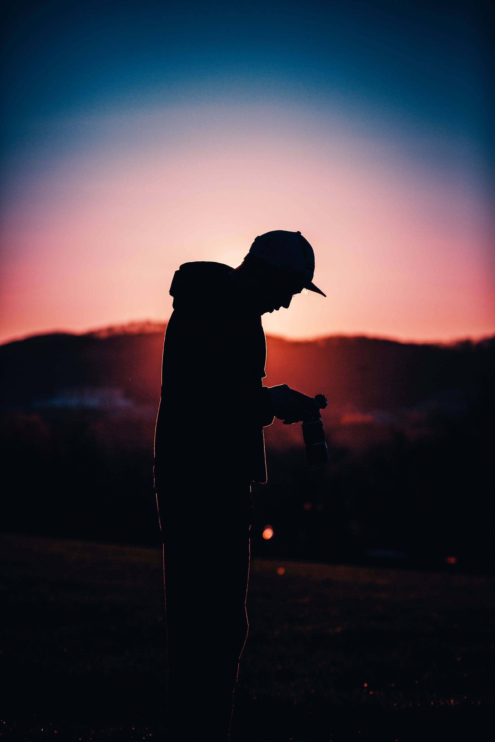 Man 桌布 壁紙 — 一個人戴著鴨舌帽，手持瓶子，背景是充滿活力的粉紅色和藍色日落天空的剪影。