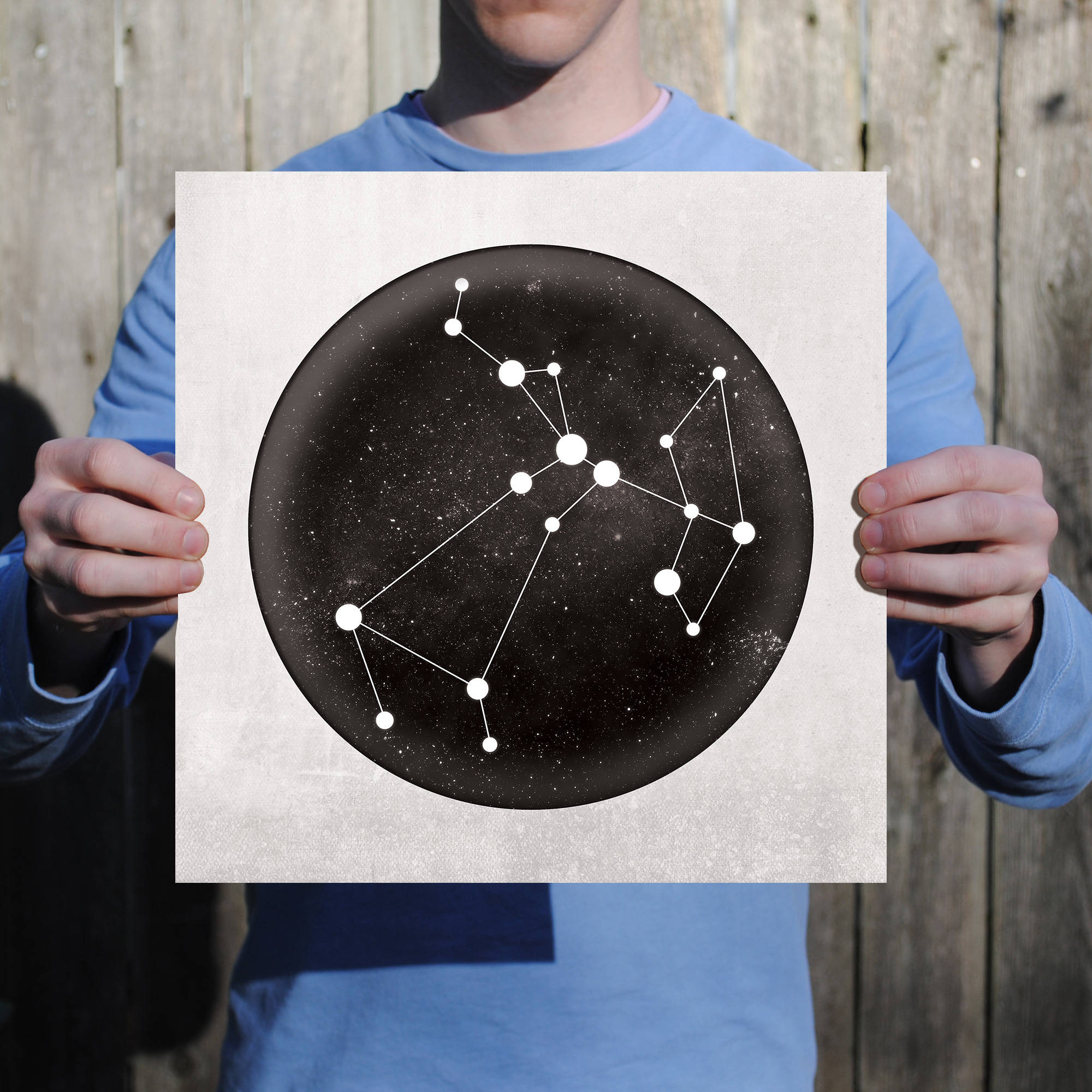 sagittarius 桌布 壁紙 — 一個人手持一張圓形海報，上面描繪了黑色星空背景上的白色線條星座，背景是木柵欄。