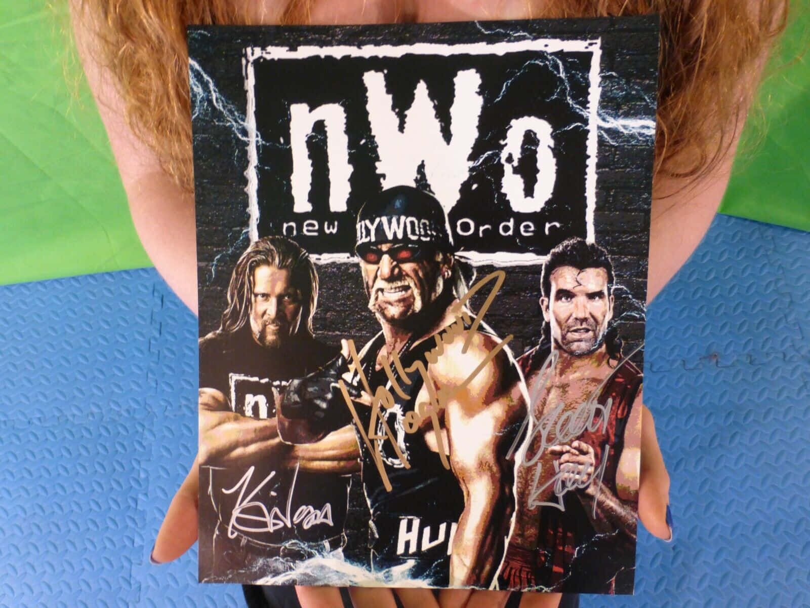 WWE 桌布 壁紙 — 一個人手持一張簽名的NWO摔角海報，上面有三個肌肉發達的摔角手，背景是黑色閃電。