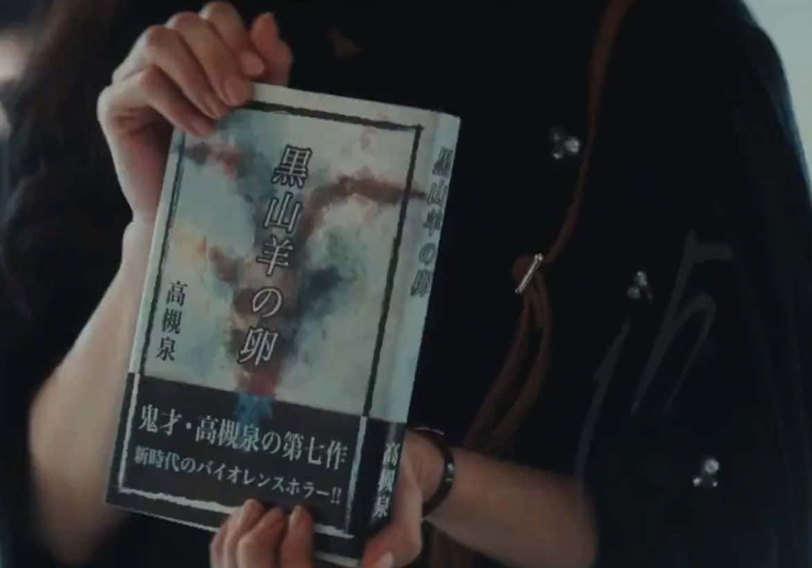 Tokyo Ghoul Movie 桌布 壁紙 — 一個人手持一本日本恐怖小說，書名為《Black Mountain Sheep's Egg》，封面為水彩畫藝術。