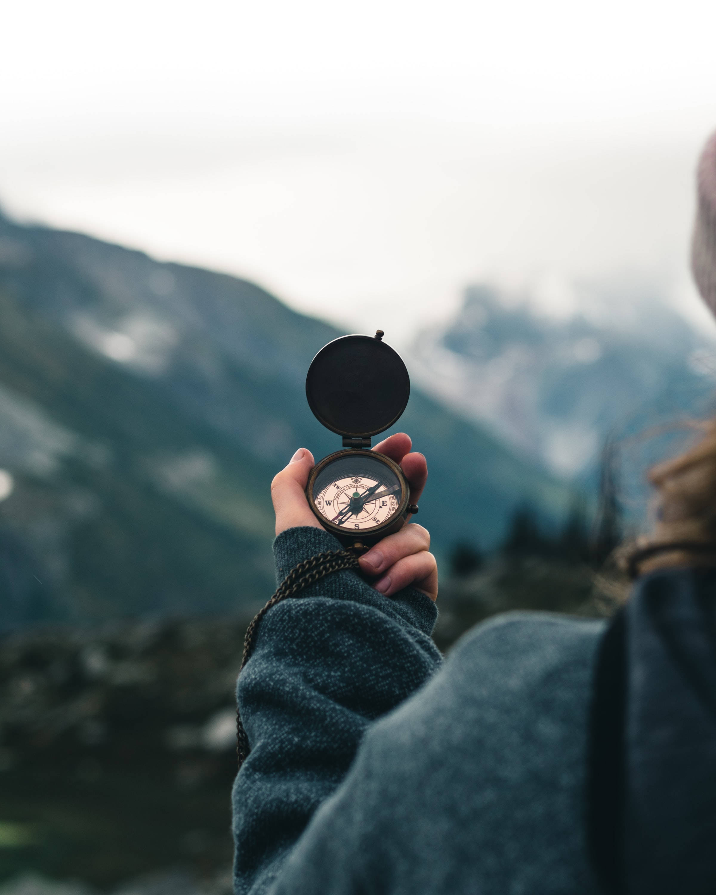 Focus 桌布 壁紙 — 一個人手持復古指南針，背景是霧氣瀰漫的山巒，在大自然中尋找方向。