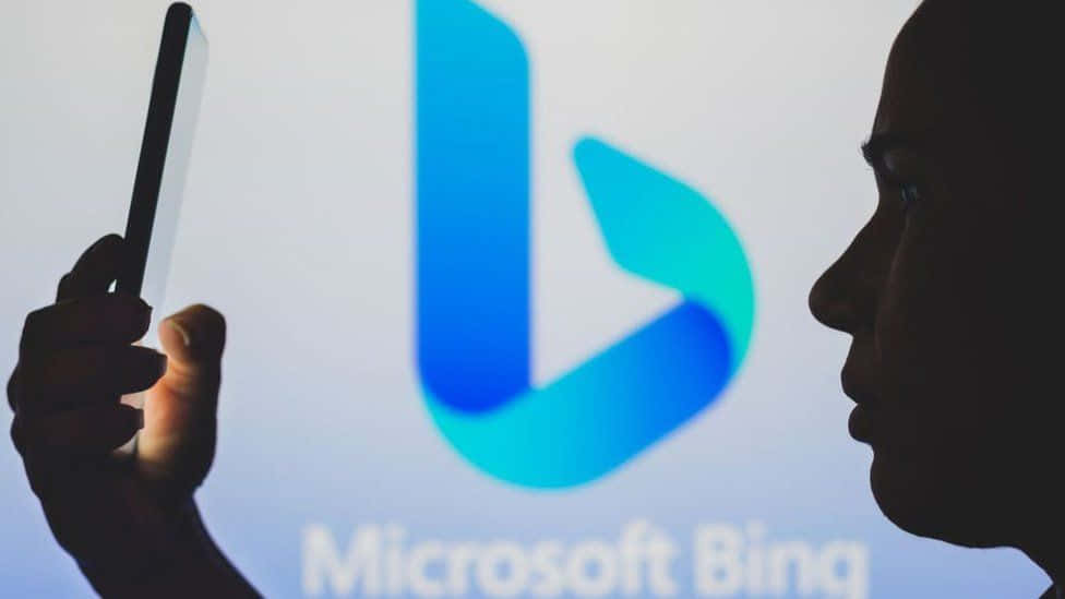 人在 Microsoft Bing 標誌投影前手持電話。 — Microsoft 壁紙