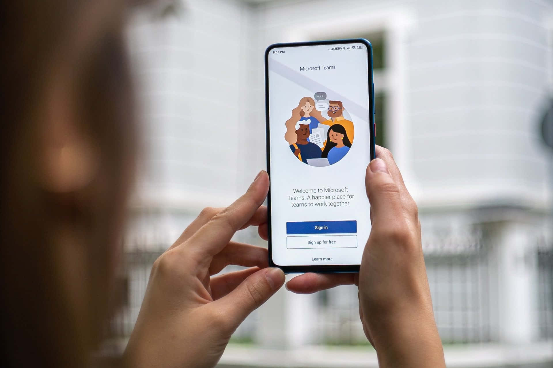 Microsoft Teams 桌布 壁紙 — 一個人手持智慧型手機，顯示Microsoft Teams歡迎畫面，上面有色彩繽紛的插圖群組和登入選項。