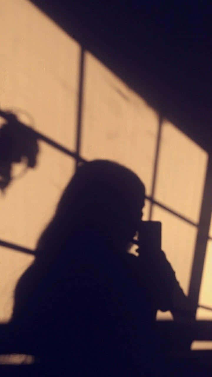 Girl Shadow 桌布 壁紙 — 一個人手持電話，背對溫暖發光的網格窗戶的剪影。