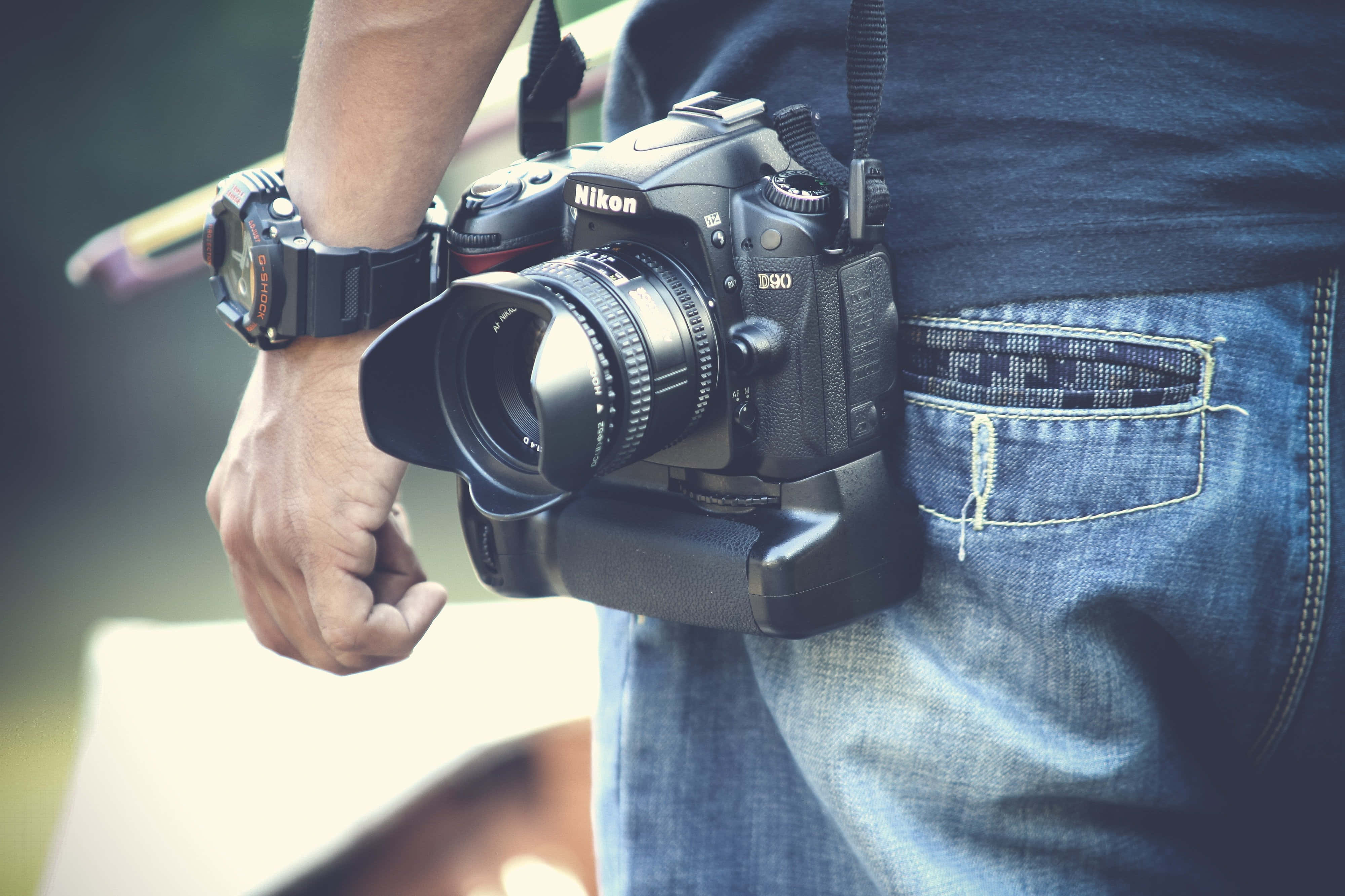攝影 桌布 壁紙 — 一個人手持黑色Nikon D80 DSLR相機，帶鏡頭和手柄，置於牛仔褲和深色T恤上。