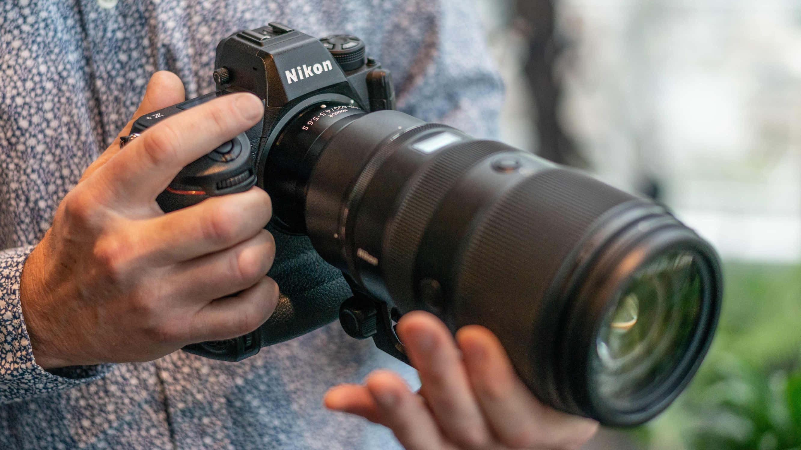 相機 桌布 壁紙 — 一個人手持黑色Nikon DSLR相機，配備大型望遠鏡頭，特寫鏡頭。