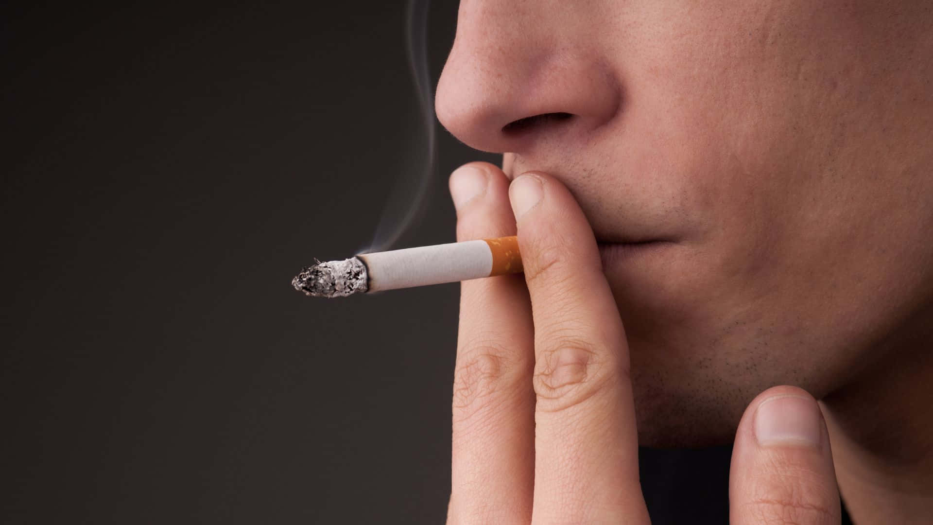 抽菸 桌布 壁紙 — 一個人手持點燃的香煙，煙霧在黑暗背景中向上繚繞的特寫。